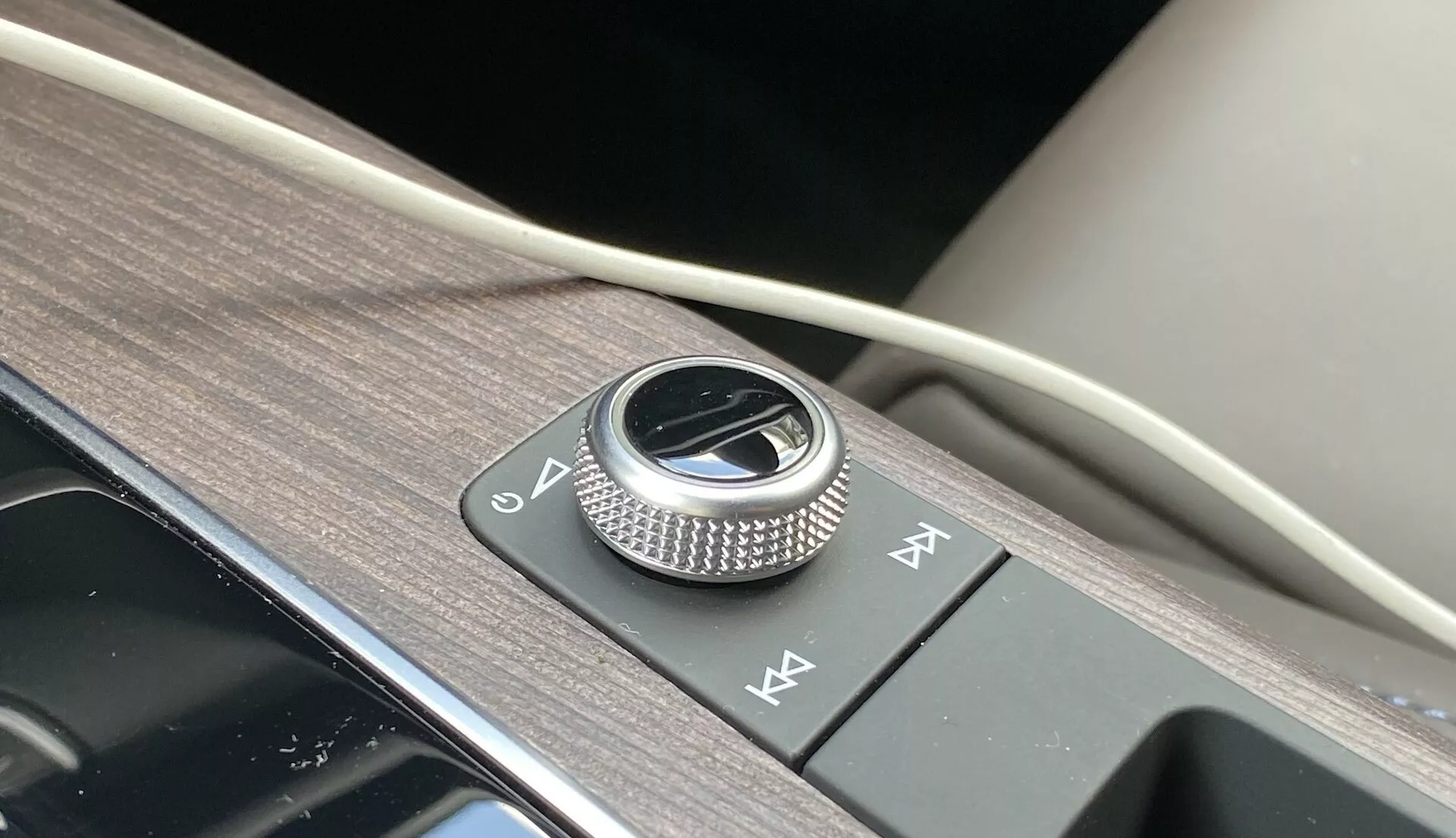 Detailný záber na stredovú konzolu Audi Q5 2020 Sportback, ktorá zvýrazňuje kovový otočný ovládač infotainmentu obklopený brúseným kovom na lesklom čiernom paneli. Vedľa sú dva tlačidlá rýchleho prístupu, všetko umiestnené na povrchu s textúrou dreva s nádychom mäkkého materiálu, čo predstavuje luxusný dizajn interiéru a pokročilé funkcie infotainment systému.