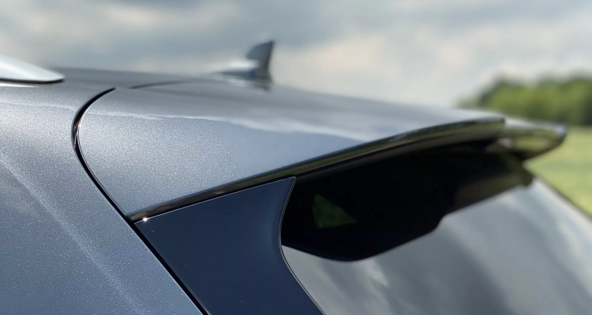 Detailný záber zadnej časti vozidla Audi Q5 2020 Sportback, zvýrazňujúci elegantný zadný spojler alebo anténu v tvare žraločej plutvy a plynulo sa zvažujúcu líniu strechy. Vozidlo má lesklý, metalický farebný povrch s vysoko kvalitnými materiálovými detailmi exteriéru. Malá hĺbka ostrosti zdôrazňuje elegantný dizajn, zatiaľ čo pozadie zostáva rozmazané.