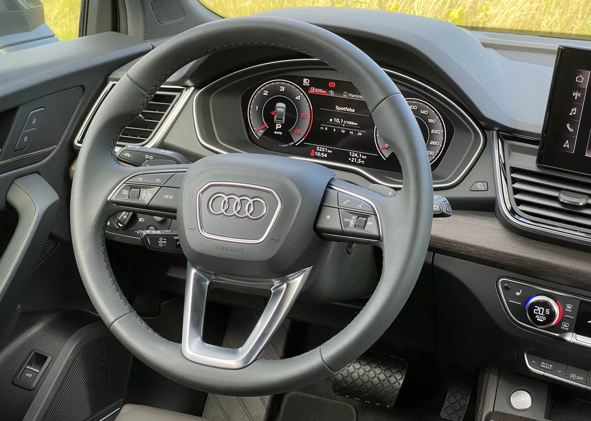 Interiér vozidla Audi Q5 2020 Sportback z pohľadu vodiča, ukazujúci volant s multifunkčnými ovládacími prvkami a emblémom Audi, digitálny prístrojový panel s rýchlomerom, otáčkomerom, centrálnym infotainment displejom a ovládacími prvkami klimatizácie, s kvalitnými mäkkými materiálmi.