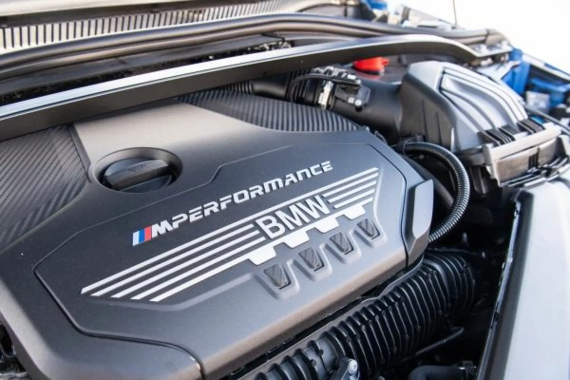 Detailný pohľad na kryt motora BMW radu 1 M Performance 2019 s logom BMW a farbami divízie M v dobre udržiavanom motorovom priestore