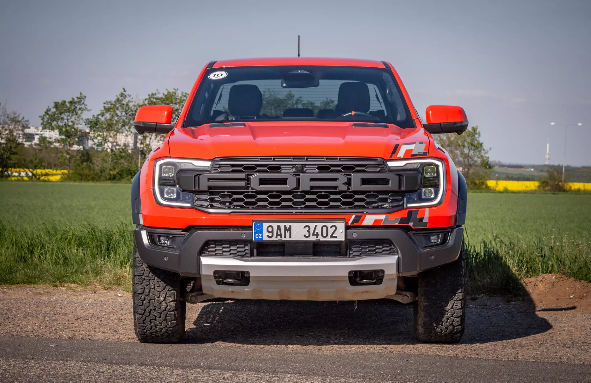 Predný pohľad na červený pickup Ford Ranger 2022 na asfalte s pozadím čistého neba, so zameraním na mriežku, LED svetlomety, predný nárazník s ťažnými háčikmi a ochrannou doskou a logom Ford