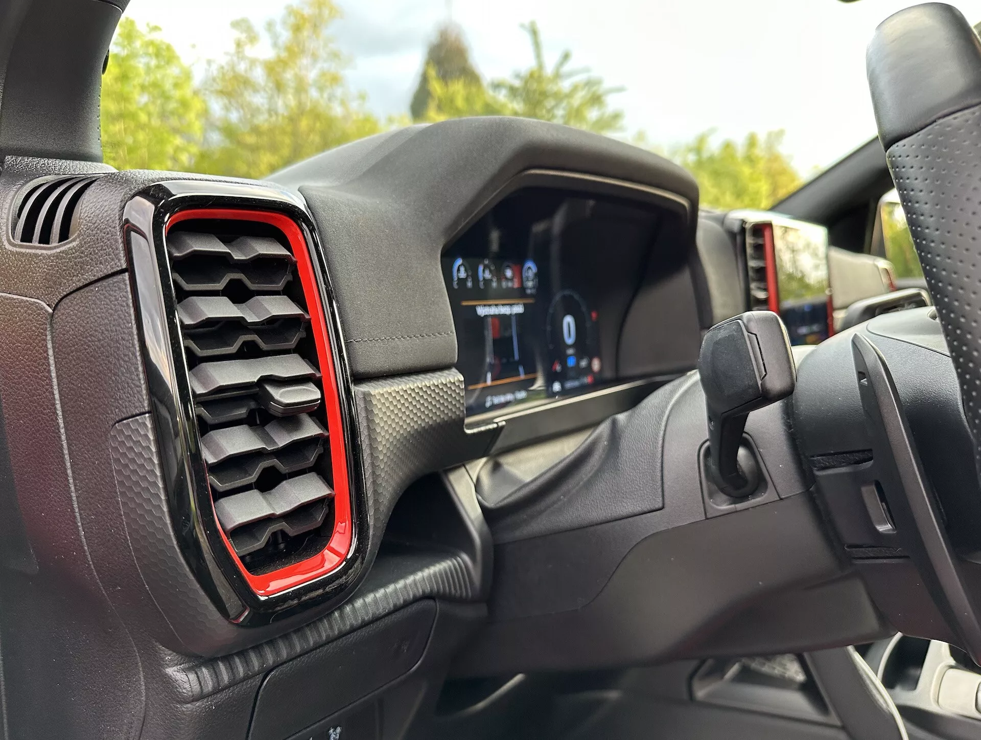 Interiér Ford Ranger 2022 z pohľadu vodiča, s digitálnym prístrojovým panelom a ľavou vzduchovou výustkou s červeným zvýraznením, s mierne excentrickým uhlom smerom k volantu naznačujúcim zatáčanie