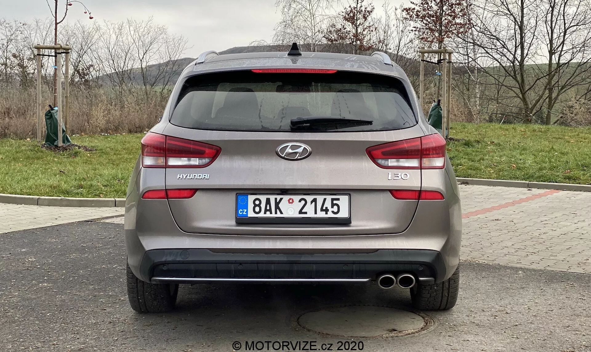 Obrázok zobrazuje zadný pohľad na Hyundai i30 Kombi z roku 2020. Auto je zaparkované a záber je urobený z priameho, priamočiareho uhlu približne vo výške kufra vozidla. S koncentrovaním na vozidlo poskytuje obrázok jasný a symetrický pohľad na zadné vlastnosti auta, vrátane loga Hyundai, názvu modelu 'i30' a vybavenia 'CRDi', ktorý označuje dieselový motor s Common Rail priamym vstrekovaním. Viditeľné detaily zahŕňajú európsku poznávaciu značku, horizontálne zadné svetla, zadné senzory, dvojité koncovky výfuku, zadný stierač, žraločiu plutvu anténu a potenciálne zadnú kameru v oblasti poznávacej značky.