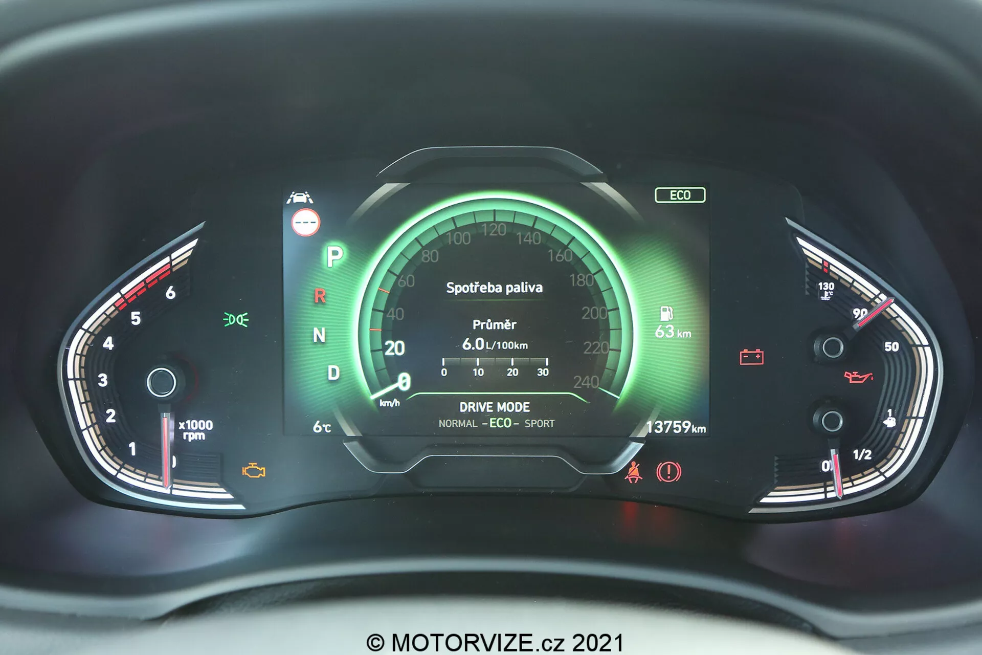 Detailný pohľad na prístrojovú dosku moderného vozidla Hyundai i30 2020 z pohľadu vodiča, s centrálnym digitálnym displejom a analógovými ukazovateľmi. Na ľavej strane je otáčkomer a na pravej strane ukazovateľ paliva a teploty motora. Rôzne indikátory a ikony zobrazujú stavy vozidla, ako sú bezpečnostný pás, stav batérie a brzdový systém. Centrálny displej zahŕňa údaje o spotrebe paliva, nastavenia režimu jazdy a odočet kilometrov. Prístrojová doska je podsvietená červenou a zelenou farbou, čo naznačuje prepracovaný elektronický systém s možnými dotykovými alebo hmatovými spätnými väzbami, vodoznak © MOTORVIZE.cz 2021.