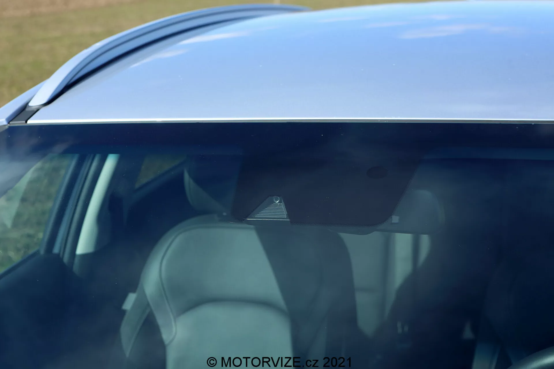 Detailný, šikmý záber zameraný na hornú polovicu bočného profilu Hyundai i30 2020. Pohľad z mierne vyvýšenej strany ukazujúci strechu vozidla, horné časti dverí a tónované okná. Línia strechy má hladký, zakrivený dizajn smerujúci k zadnému spojleru alebo žraločej anténe. Čiastočný pohľad na bočné okná ponúka pohľad na svetlý interiér sedadiel, opierky hlavy a priestoru pre cestujúcich. Odraz oblohy na streche a oknách naznačuje jasné prostredie. Značka vody © MOTORVIZE.cz 2021 naznačuje, že fotografia bola urobená na účely recenzií alebo propagácie.