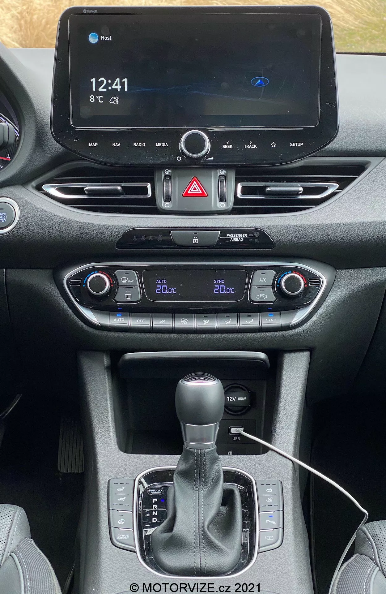Pohľad spredu na centrálnu konzolu Hyundai i30 Kombi 2020 z predných sedadiel, zobrazujúci digitálny infotainment systém s časom (12:41), teplotou (8°C) a ikonou Bluetooth. Dole nájdete tlačidlo výstražného signalizácie, dvojzónovú klimatizáciu s oddeleným nastavením teploty (vodič 22°C, spolujazdec 20°C), tlačidlo štart-stop, automatickú radiacu páku s manuálnym režimom, potenciálne držiaky na nápoje/úložný priestor, port na pripojenie s viditeľným káblom a zmiešaný materiálový dizajn prístrojovej dosky a konzoly. Dole je autorský vodoznak '@ MOTORVIZE.cz 2021'.