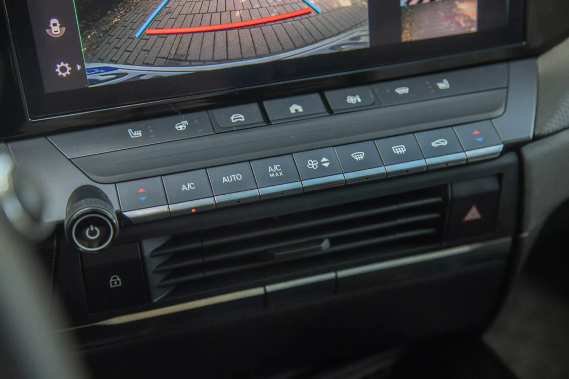 Centrálna konzola a panel klimatizácie Opel Astra 2022, zdôraznenie ovládača teploty, rýchlosti ventilátora, distribúcie vzduchu a tlačidiel automatickej klimatizácie s digitálnym displejom zobrazujúcim zadnú kameru