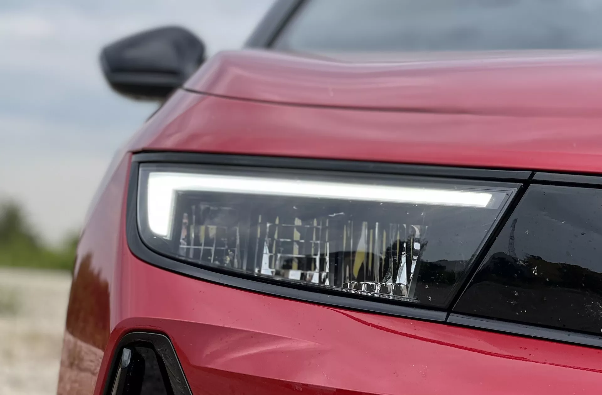Detailný pohľad z prednej strany na červený Opel Astra 2022 s dôrazom na podrobný dizajn LED svetlometu, ktorý ukazuje modernú technológiu osvetlenia a obrysy vozidla