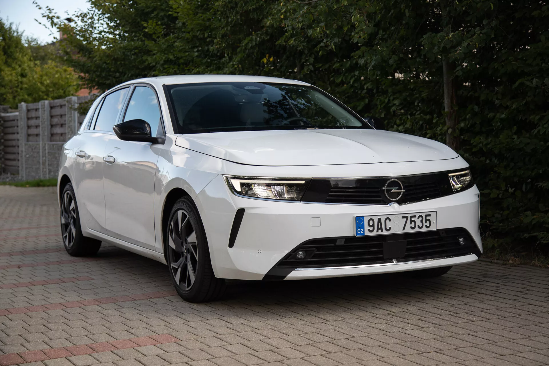 Opel Astra 2022 zachytená v predmestskom prostredí, prezentujúca svoje štíhle svetlomety, výraznú prednú mriežku, aerodynamický dizajn vrátane viacerých hovorí zliatinových kolies a inovatívnu technológiu z trojštvrtečného predného pohľadu