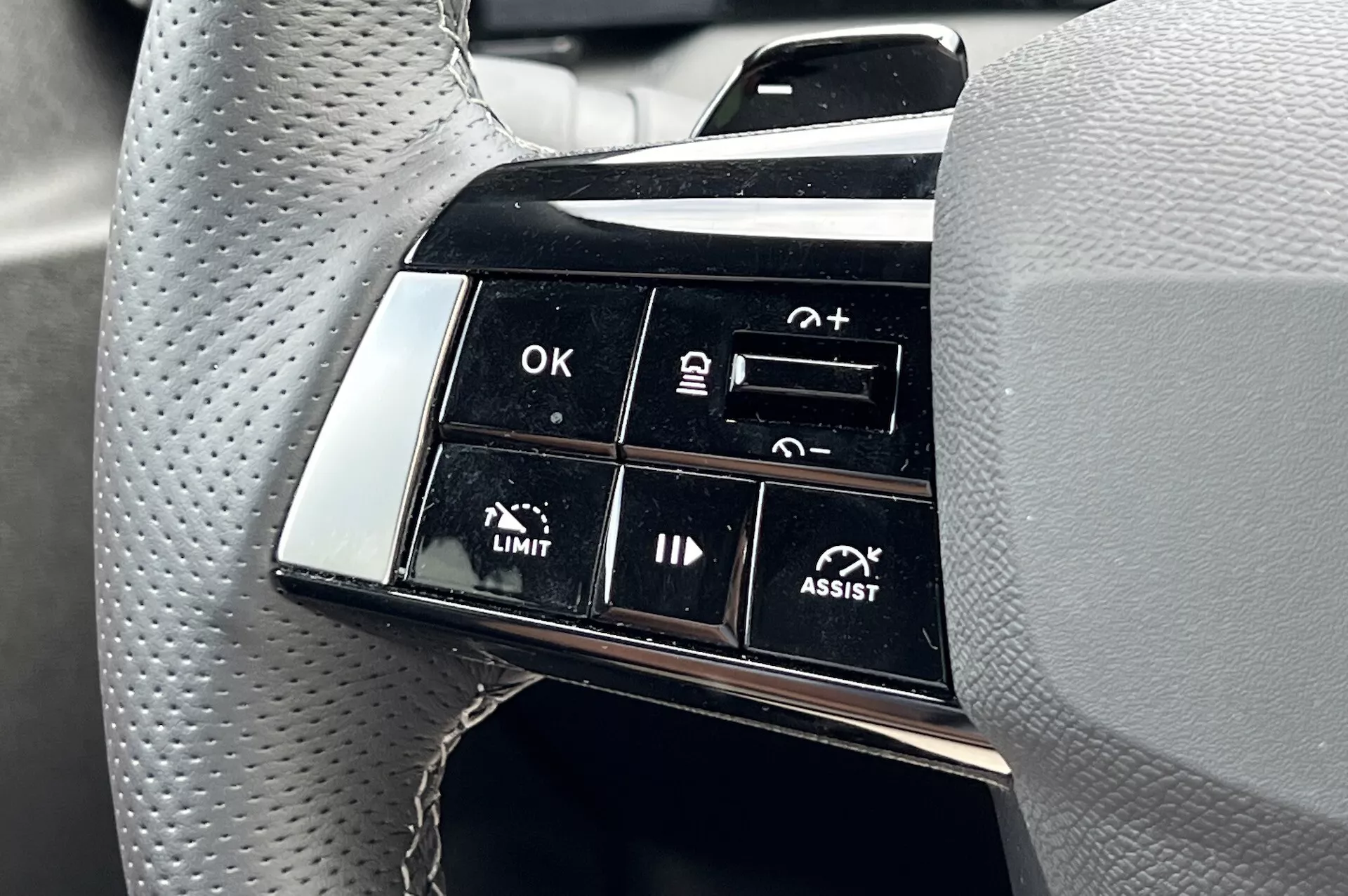 Detailný pohľad na zoskupenie tlačidiel na volante Opel Astra 2022 zdôrazňujúce pokročilé funkcie asistenčných systémov pri jazde, vrátane adaptívneho tempomatu a systému udržiavania jazdného pruhu, so zameraním na popisy funkcií ako OK, +, -, LIMIT a ASSIST z pohľadu vodiča