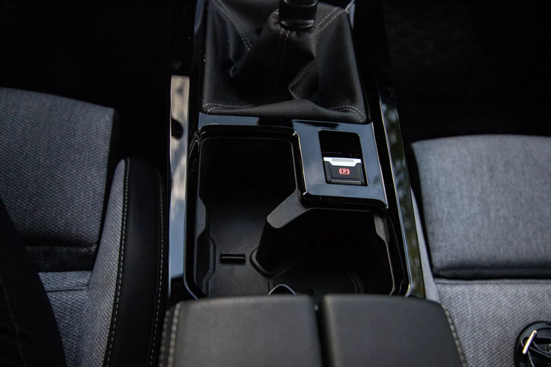 Detail stredovej konzoly Opel Astra 2022 ukazujúci otvorený úložný priestor, čalúnenie látkou, manuálnu radiacu páku s perforovanou kožou, USB port a vnútorné osvetlenie