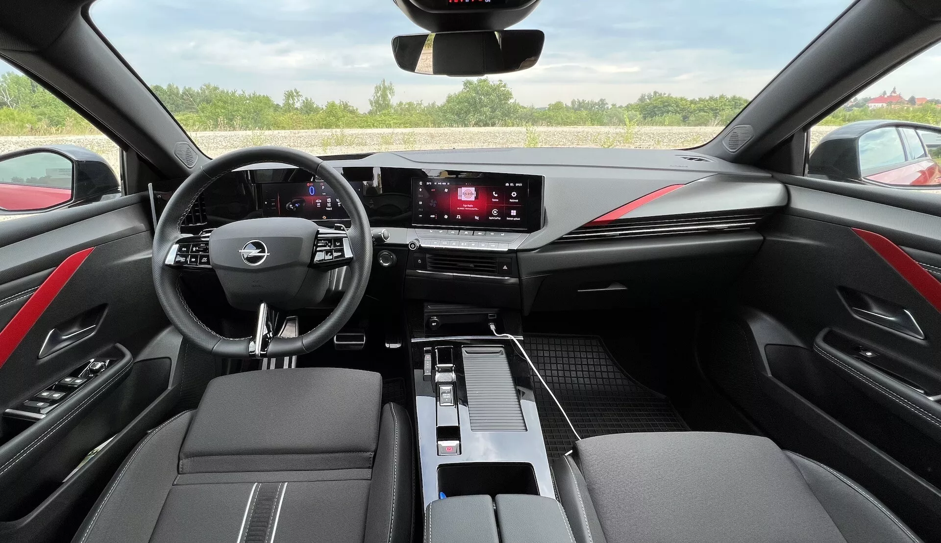 Interiér Opel Astra 2022 predstavujúci multifunkčný volant s tromi ramenami, digitálny prístrojový panel, dotykový informačný systém, elegantné ovládače klímy, dvojfarebné čierno-červené kožené dokončenie a moderný dizajn kabíny z pohľadu vodiča