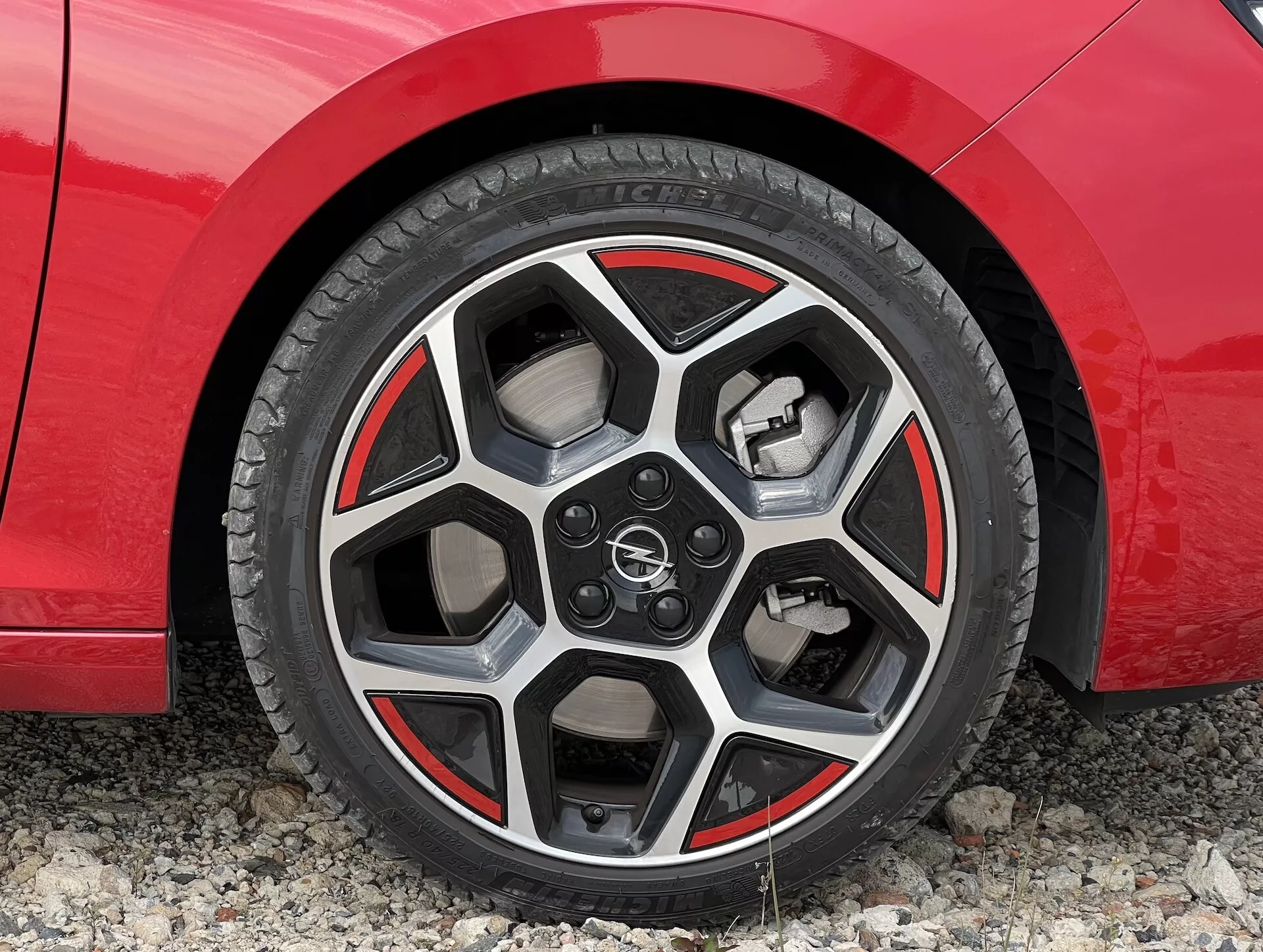 Detailný pohľad na koleso červeného auta Opel Astra 2022, ukazujúci dizajn zliatiny, dezén pneumatiky a systém výkonných bŕzd