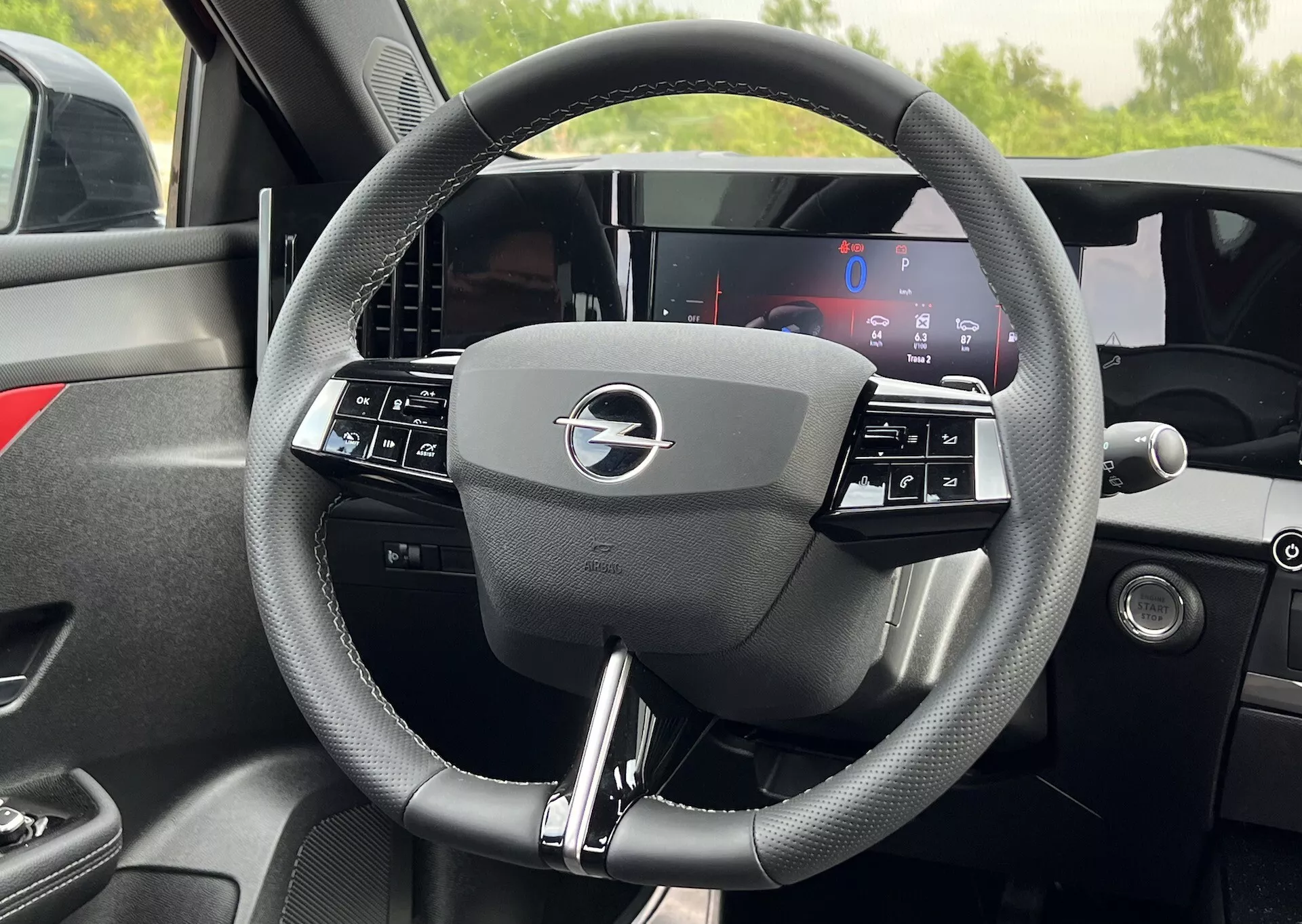 Detailný vnútorný pohľad na volant Opel Astra 2022 s trojspoke dizajnom s integrovanými ovládacími prvkami a úplne digitálnym displejom palubnej dosky za ním, zdôrazňujúci moderné vozidlové technológie a ergonómiu