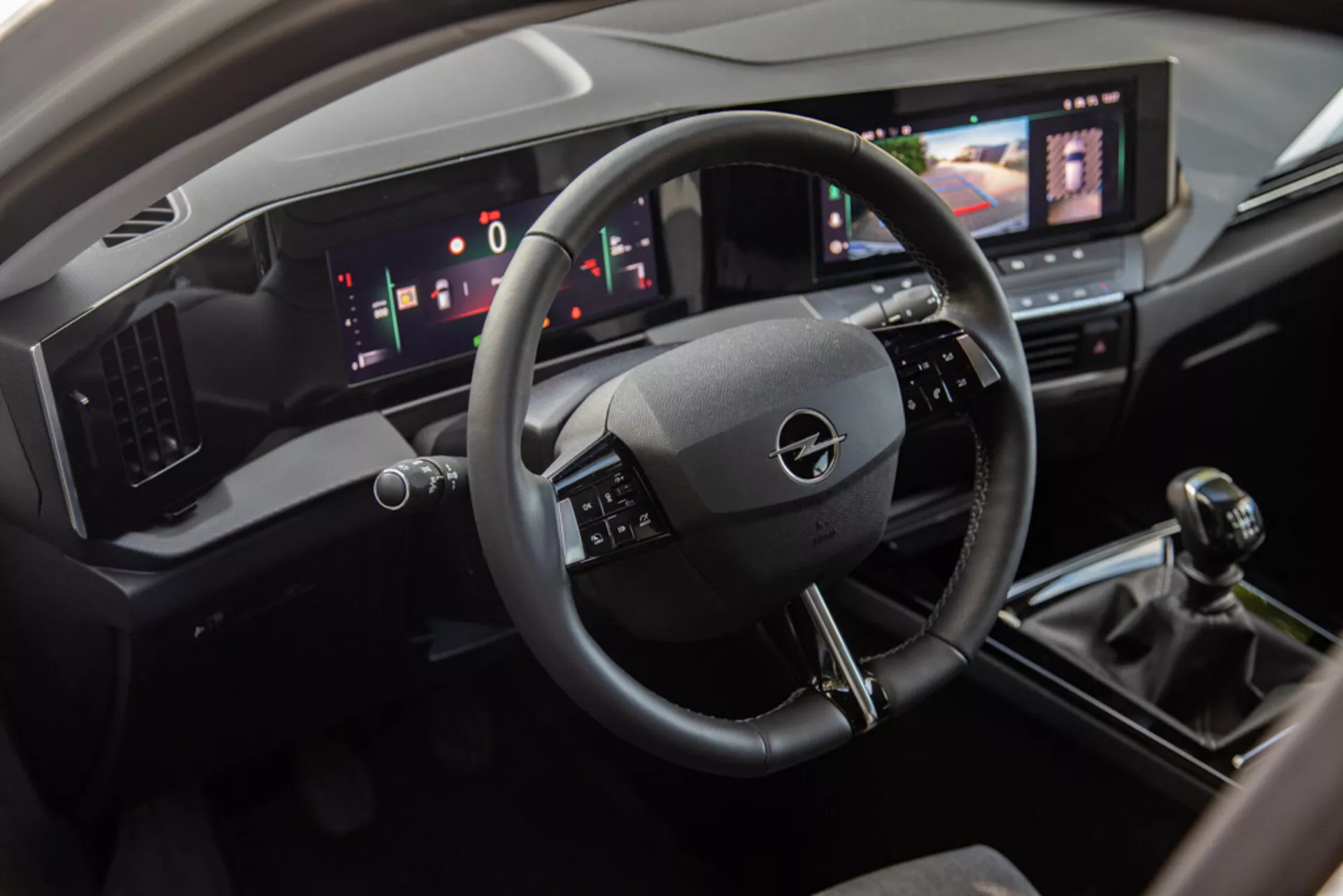 Interiér Opel Astra 2022 s pohľadom na priestor vodiča s trojspoke volantom, digitálnym prístrojovým panelom a centrálnou konzolou vrátane dotykového informačno-zábavného systému, manuálnej prevodovky a moderných ovládacích prvkov klimatizácie