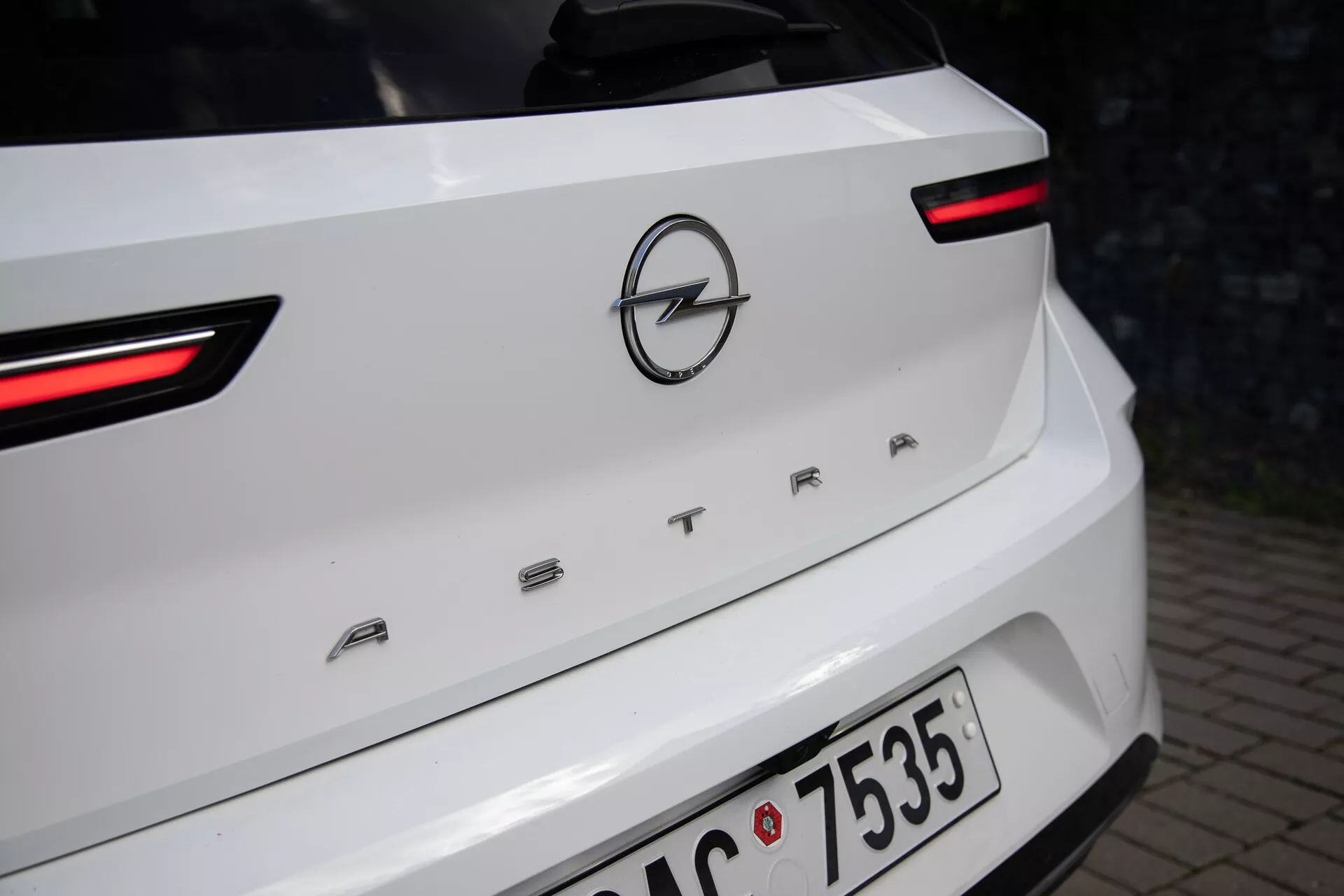 Detailný pohľad na zadnú časť bieleho Opelu Astra ročník 2022, zvýrazňujúci LED zadné svetlá, logo Opel a názov modelu 'ASTRA' na veku batožinového priestoru