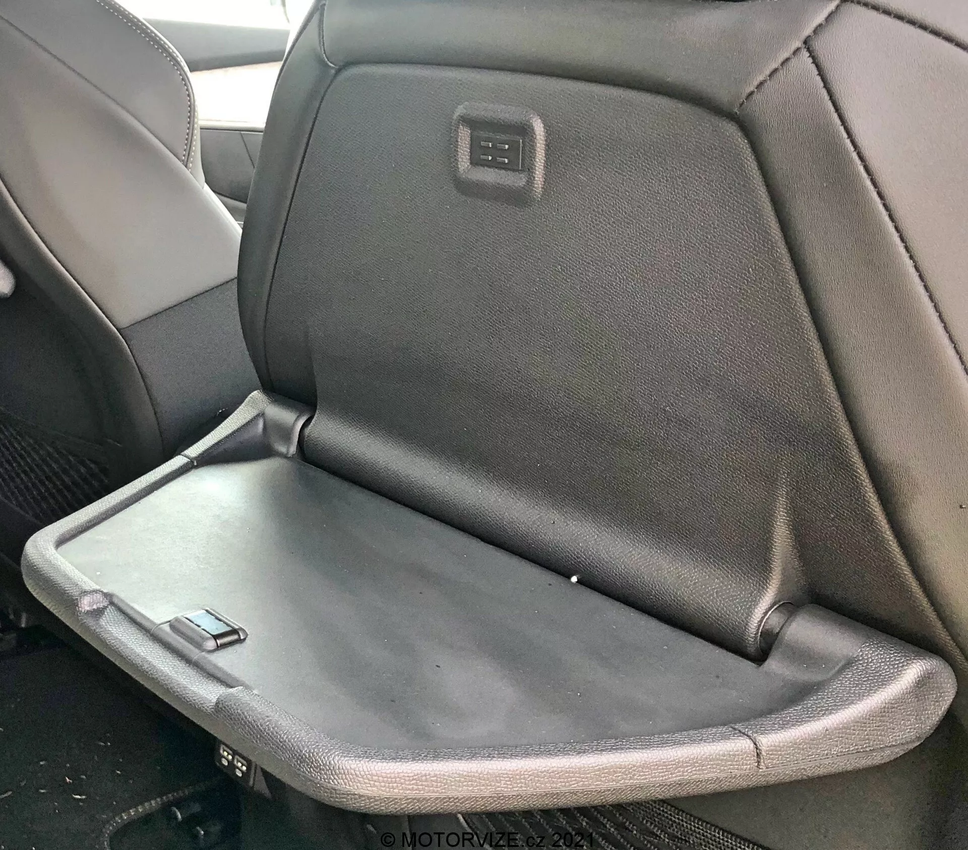 Interiér vozu Peugeot 5008 2021 s detailným pohľadom na zadné sedadlo, ktoré obsahuje sklopnú opierku alebo odkladací stolík, s kombináciou látkového a koženého čalúnenia a integrovaným displejom či ovládacím panelom na zadnej strane opierky hlavy predného sedadla.