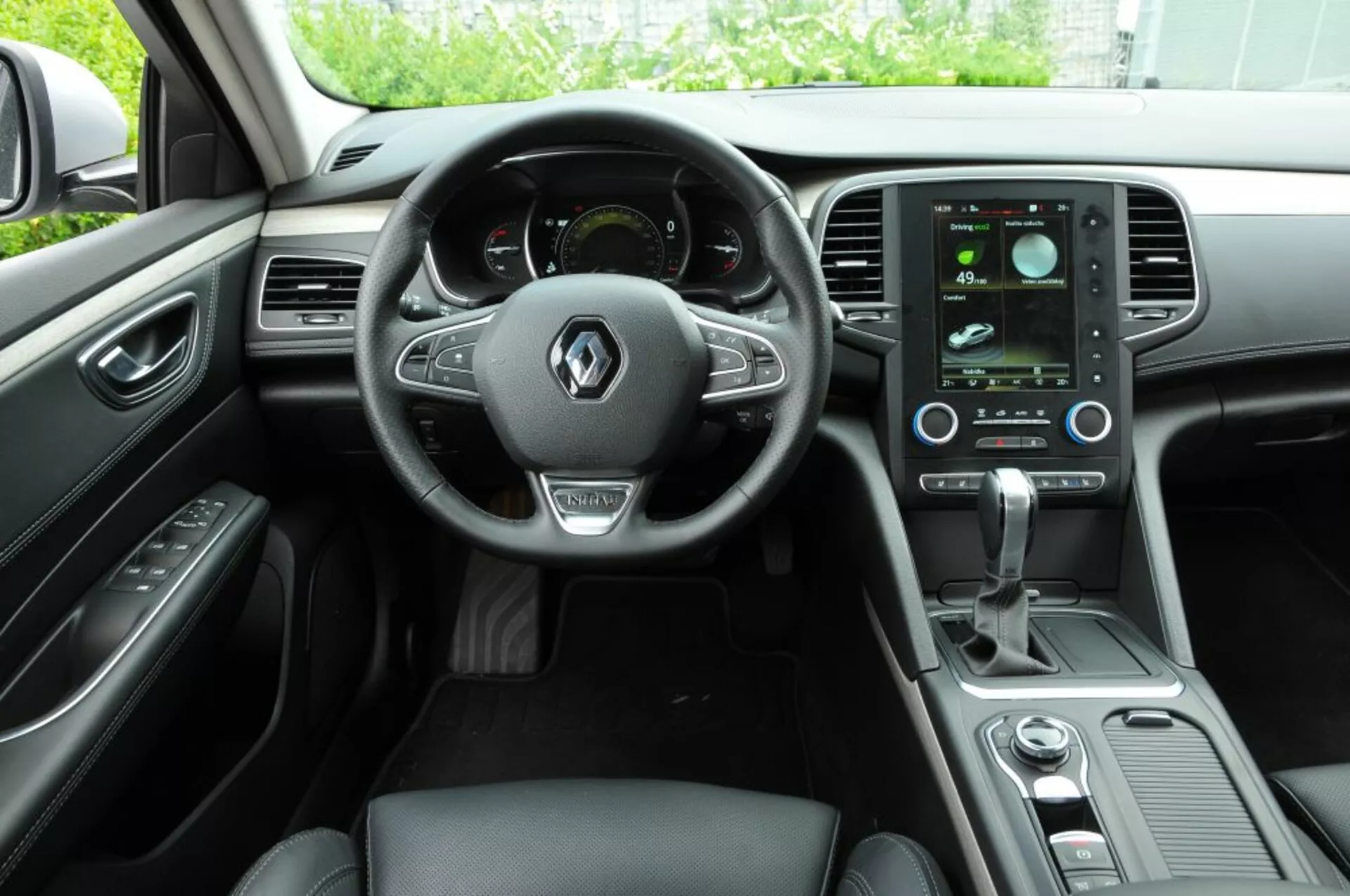 Interiér Renault Talisman 2016 predstavuje kokpit vodiča s multifunkčným koženým volantom, digitálnym prístrojovým panelom, vertikálnym dotykovým infotainment systémom a elegantnými ovládačmi klímy z pohľadu zadného cestujúceho