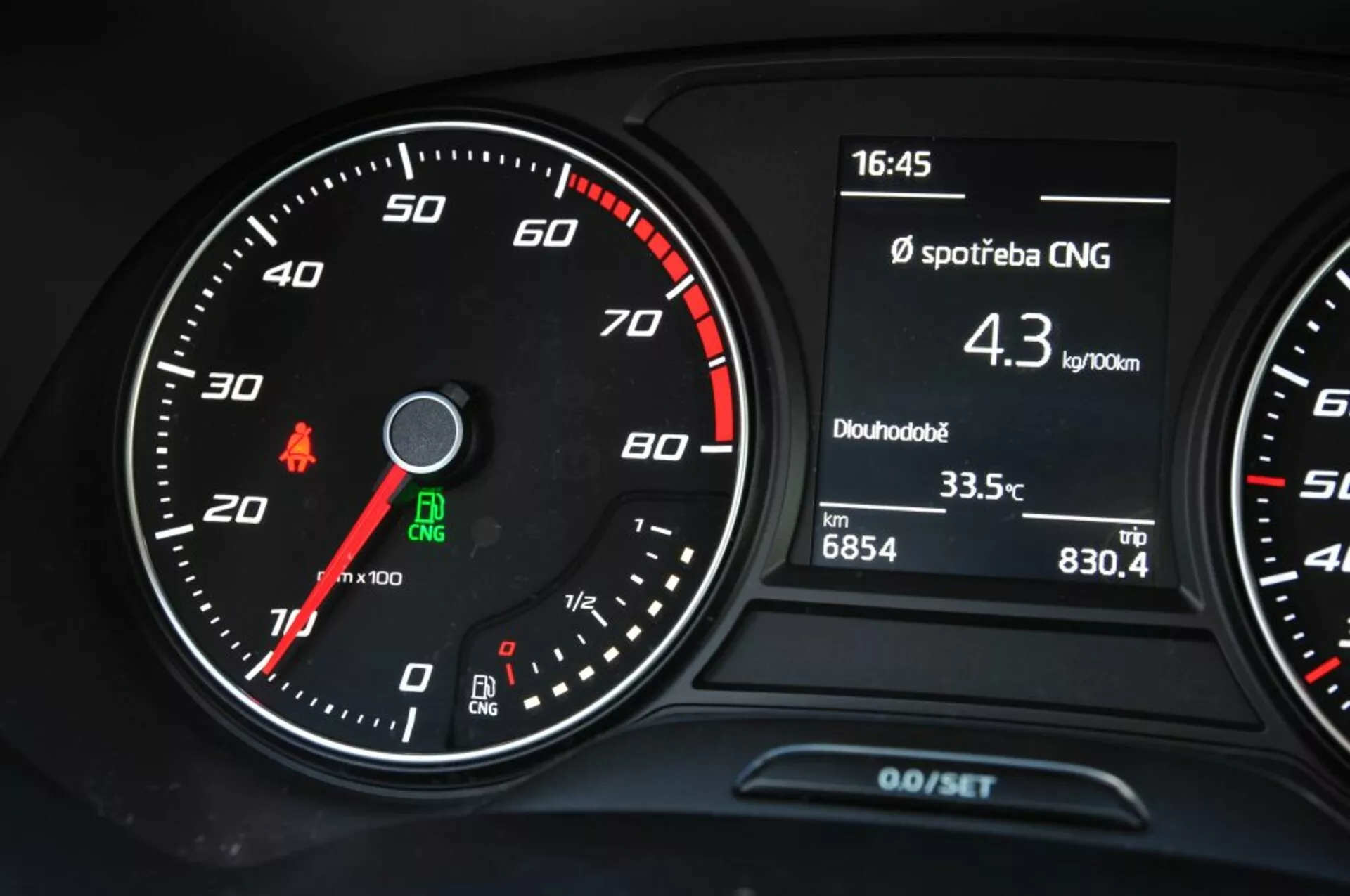 Detailný pohľad na prístrojovú dosku Seat Leon SC z roku 2016, zobrazujúci analógový rýchlosťomer, otáčkomer a multifunkčný displej s údajmi o spotrebe CNG, čase, teplote a údajoch o odometeri cesty