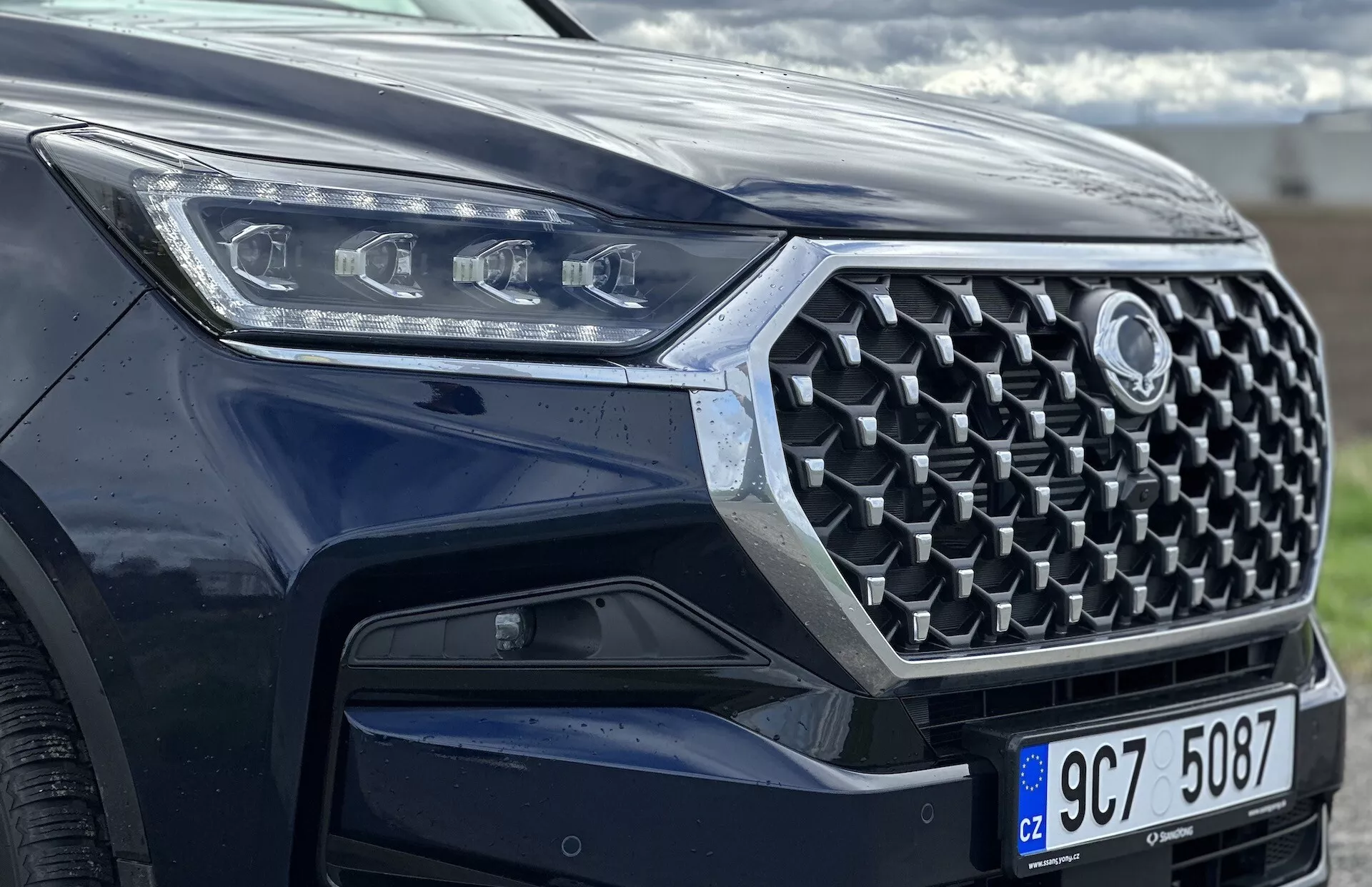 Pohľad z predného uhla na SsangYong Rexton 2021 so zameraním na mriežku, predný nárazník a dizajn LED svetlometov, ukazujúci pokročilé bezpečnostné funkcie a modernú technológiu s metalickým lakom.