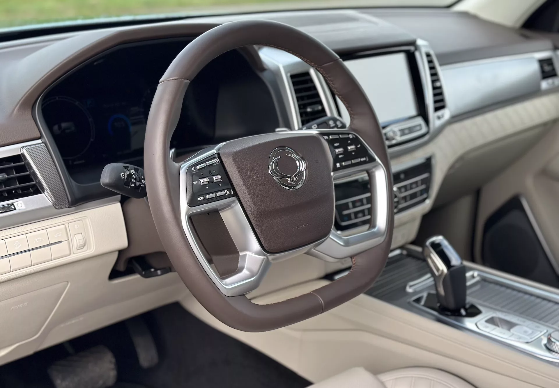 Luxusný interiér SsangYong Rexton 2021 z pohľadu spolujazdca, s multifunkčným koženým volantom s kovovými akcentmi, digitálnym prístrojovým panelom, pokročilým informačným systémom a dvojfarebnou schémou béžovej a tmavej farby.