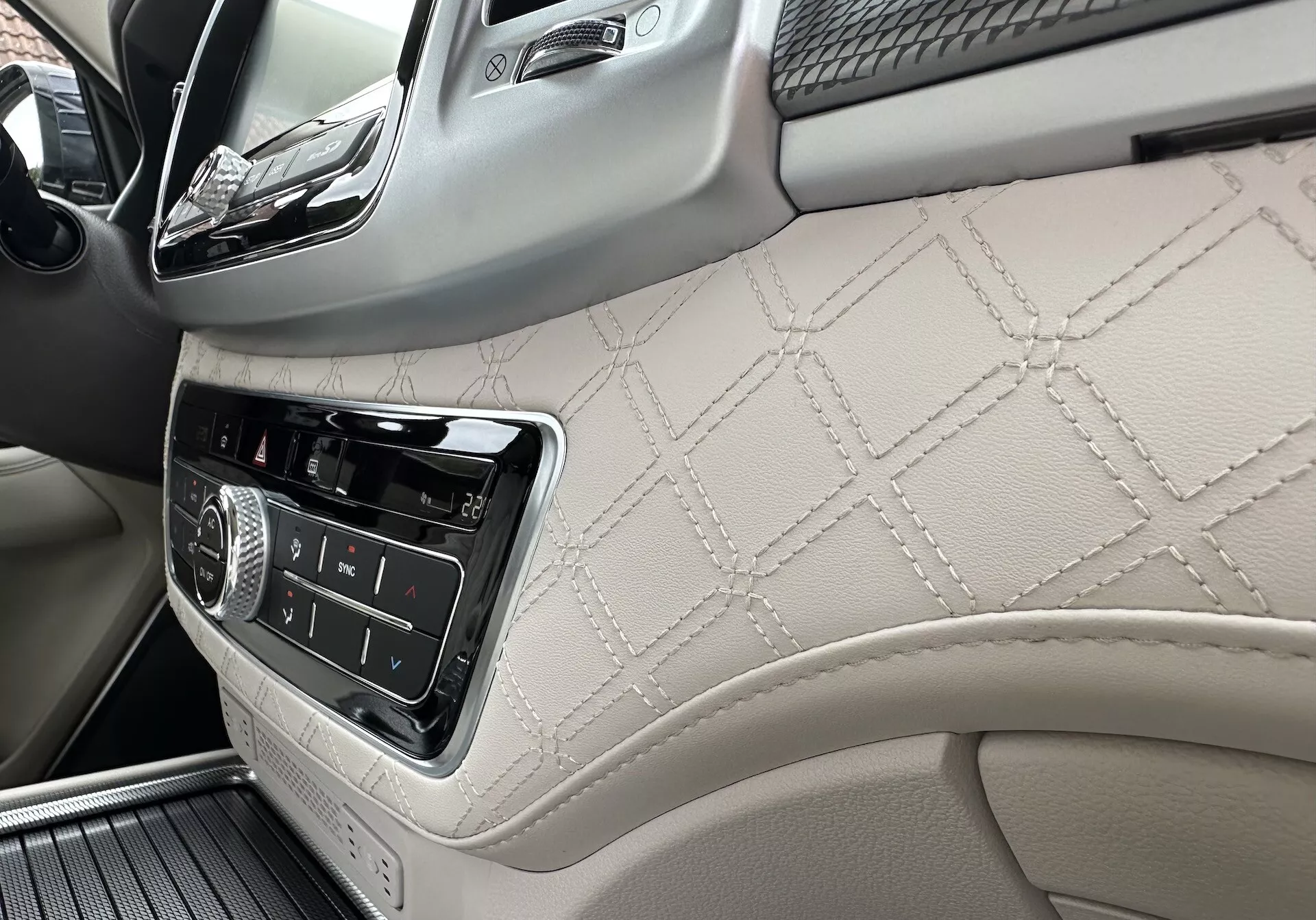 Interiér SsangYong Rexton 2021 so zameraním na palubnú dosku na strane spolujazdca a časť predného dverového panela s kožou s diamantovým prešívaním, ovládacími prvkami infotainmentu a luxusnými drevenými detailmi