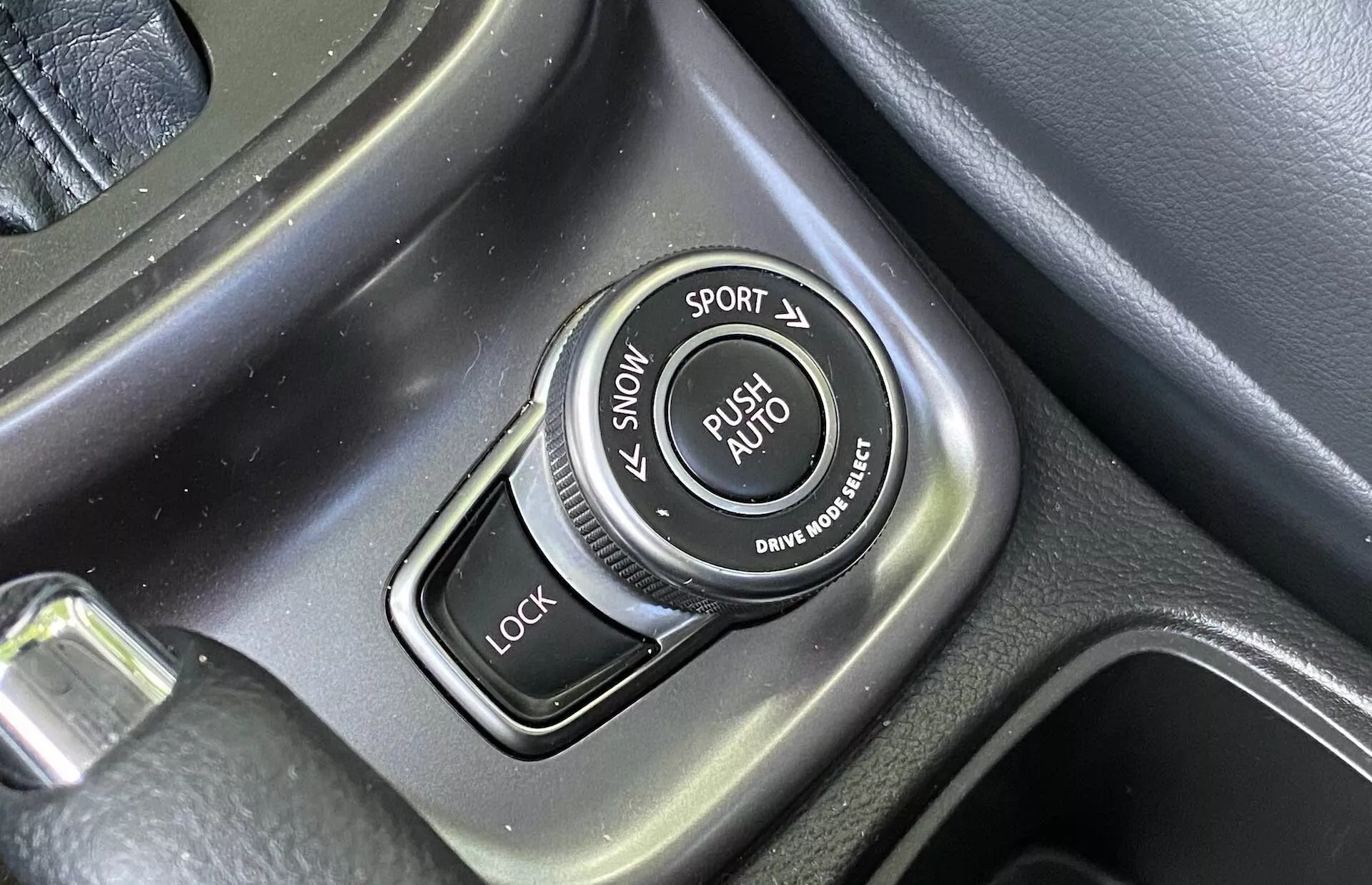 Detailný záber na volič jazdných režimov v strednej konzole Suzuki Vitara 2018 s označeniami pre režimy SNOW, SPORT, LOCK a AUTO, textúrovaným obvodom a kartáčovanými kovovými akcentmi.