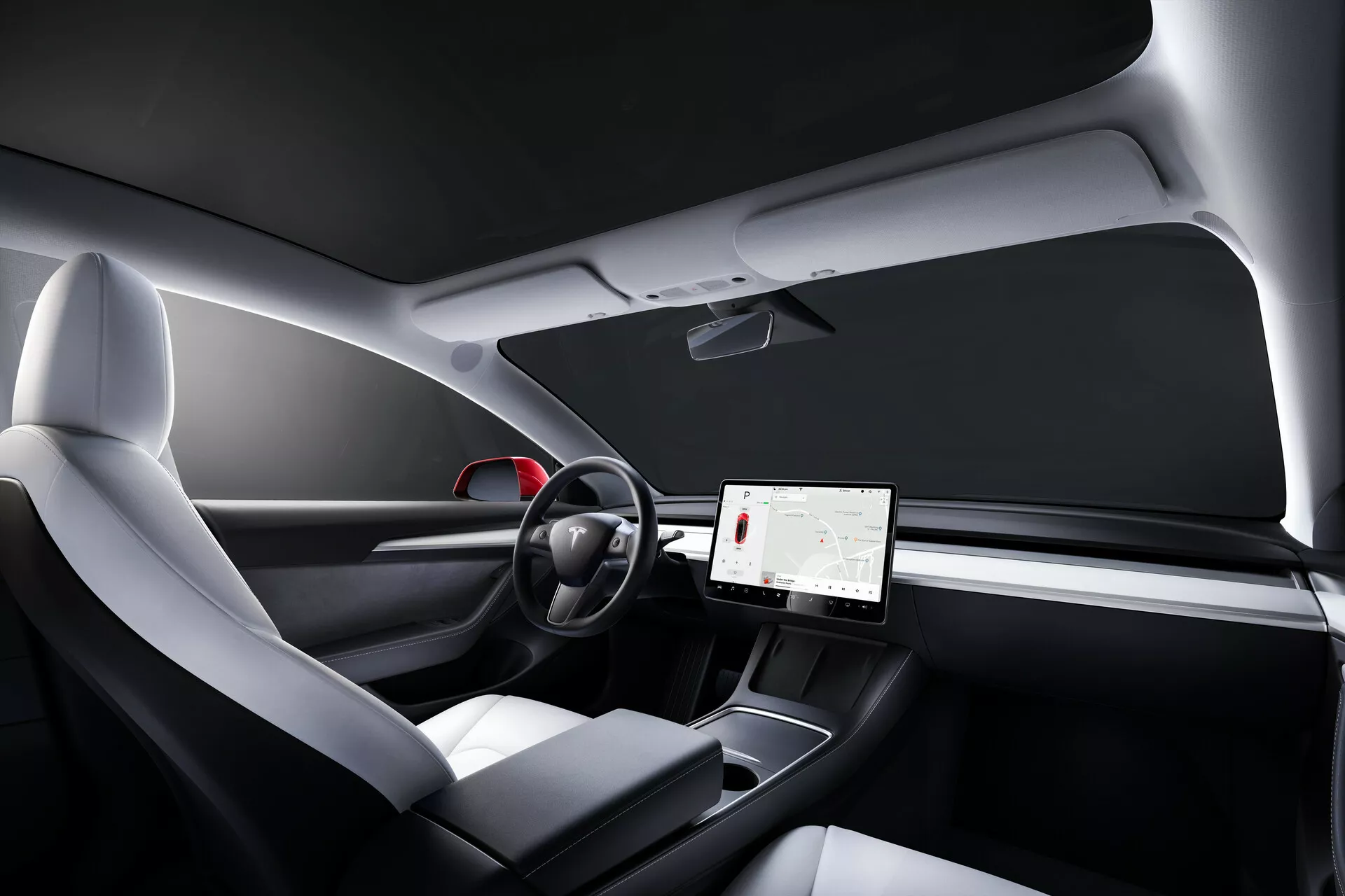 Vnútorný záber Tesly Model 3 2019 (1. generácia) z pohľadu spolujazdca, ktorý zobrazuje minimalistický dizajn palubnej dosky, veľký centrálny dotykový displej, dvojramenný volant s dotykovými ovládačmi, moderné ergonomické sedadlá s kombinovaným čalúnením, zjednodušenú stredovú konzolu, drevopodobné dekoratívne prvky a panoramatickú sklenenú strechu.