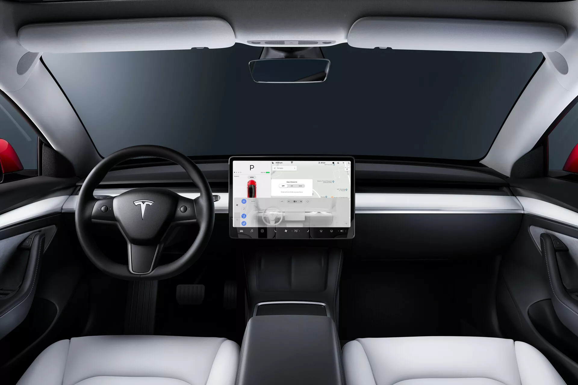 Interiér Tesla Model 3 prvej generácie z roku 2019, pohľad zo zadného sedadla, zobrazujúcej minimalistickú palubnú dosku s veľkým centrálnym dotykovým displejom. Dvojramenný volant s emblémom Tesla, dvojfarebná farebná schéma s bielymi sedadlami a čiernymi akcentmi, moderný dizajn sedadiel, úzke vetracie štrbiny a absencia viditeľných ukazovateľov naznačujú sofistikovanú technologickú integráciu a dizajn elektrického vozidla.