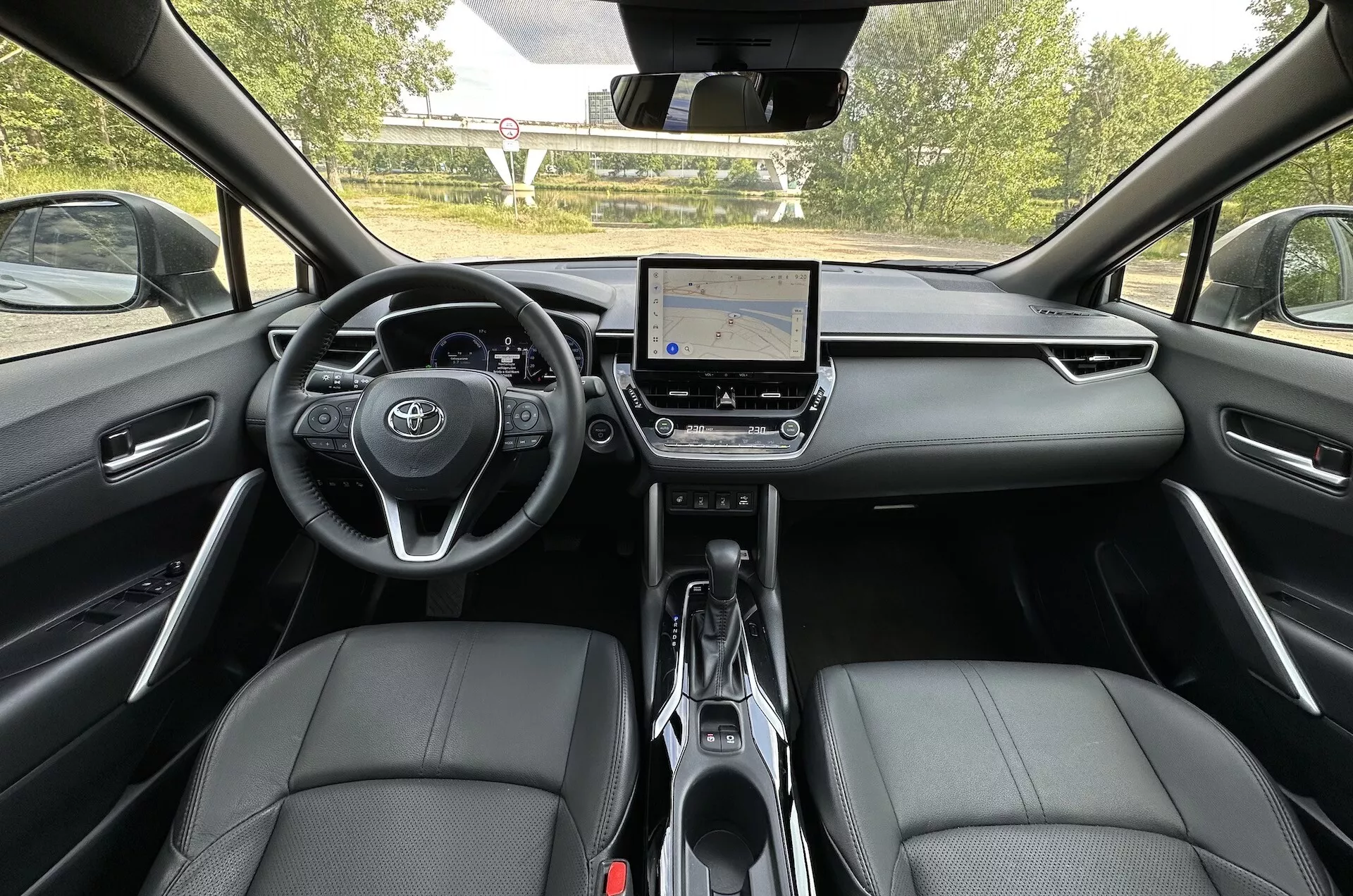 Interiér Toyota Corolla Cross 2022 z pohľadu zo zadného sedadla, ukazujúce palubnú dosku, dotykový informačný systém a predné sedadlá pokryté kožou