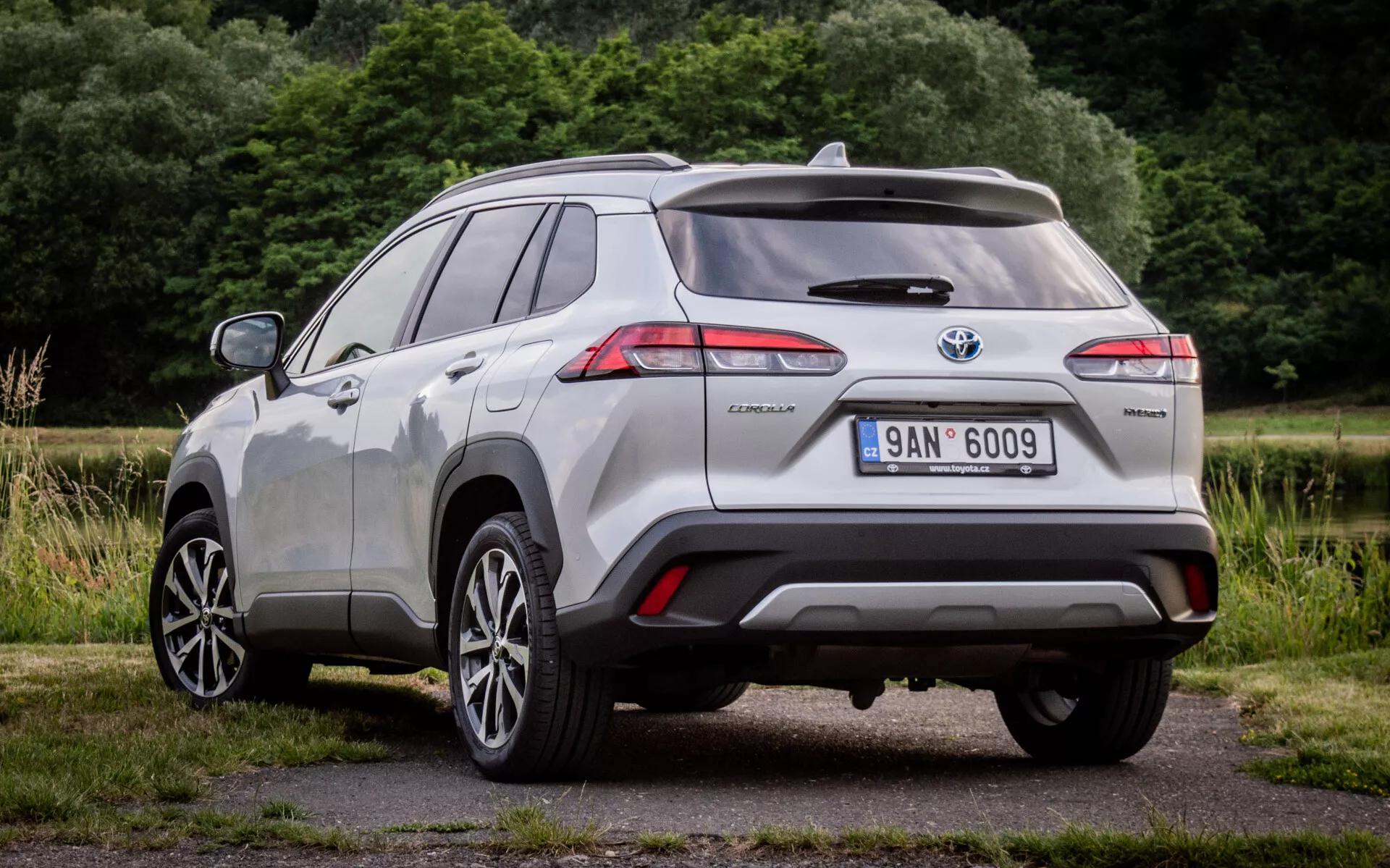 Zadný trojštvrtečný pohľad na Toyota Corolla Cross 2022 ukazujúci LED zadné svetlá, odznak hybridu a senzory asistencie pri parkovaní