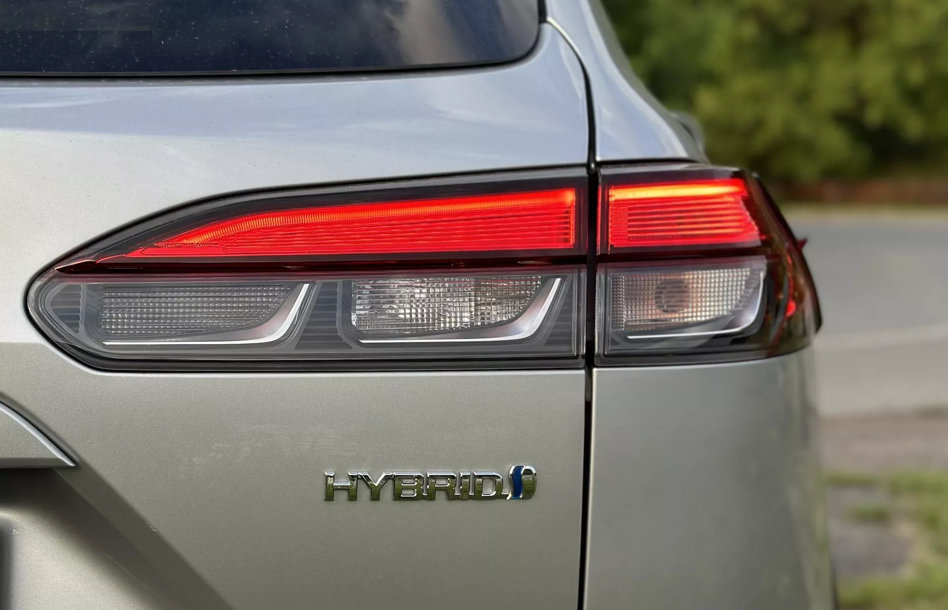 Detailný záber na zadný ľavý roh Toyota Corolla-Cross 2022 zobrazujúci dizajn LED zadného svetla a emblém HYBRID so zameraním na environmentálne priateľskú technológiu vozidla a lesklý povrch v tlmenom svetlo šedej farbe