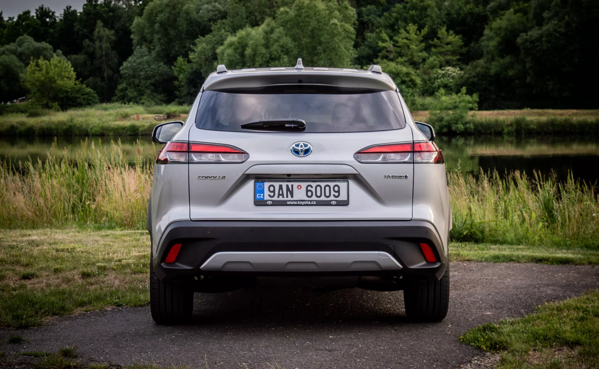 Zadný pohľad na hybridný model Toyota C-HR s LED zadnými svetlami, integrovaným nárazníkom s difúzorom a odrazkami, anténou na streche a zliatinovými kolesami na prírodnom pozadí