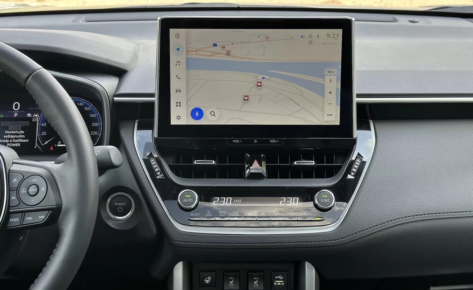 Interiér Toyota Corolla Cross 2022 ukazuje modernú stredovú konzolu s veľkým, vertikálnym dotykovým displejom pre navigáciu, obklopeným elegantnými prvkami palubnej dosky vrátane detailov z kože, digitálnym prístrojovým panelom vedľa volantu a ergonomickými dotykovými ovládačmi pre klimatizáciu a zvuk, v prirodzenom osvetlení.