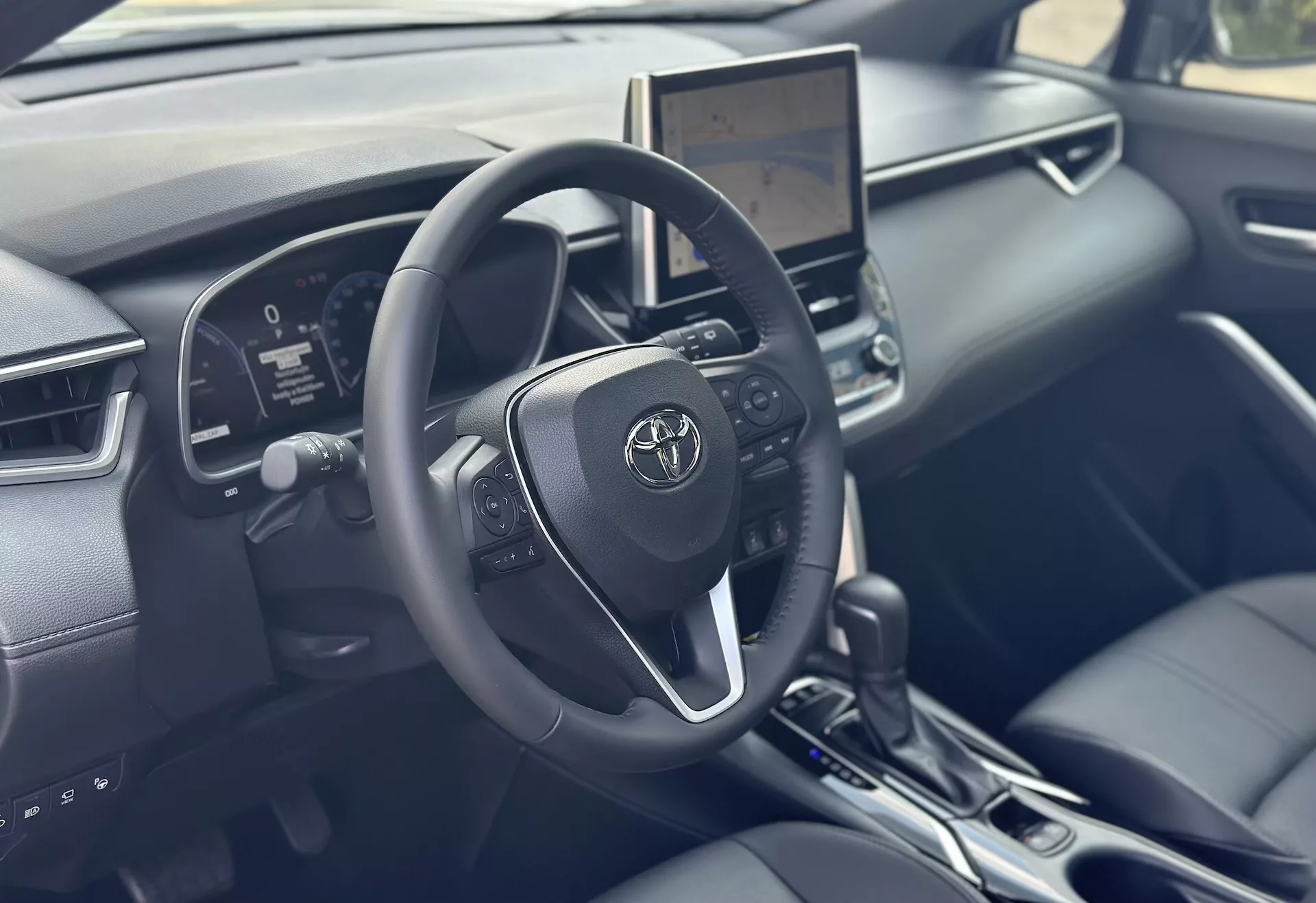 Interiér Toyoty Corolla Cross 2022 so zameraním na stranu vodiča s detailným volantom, digitálnym prístrojovým panelom a centrálnym dotykovým infotainmentom s modernou technológiou a akcentmi z čiernej kože