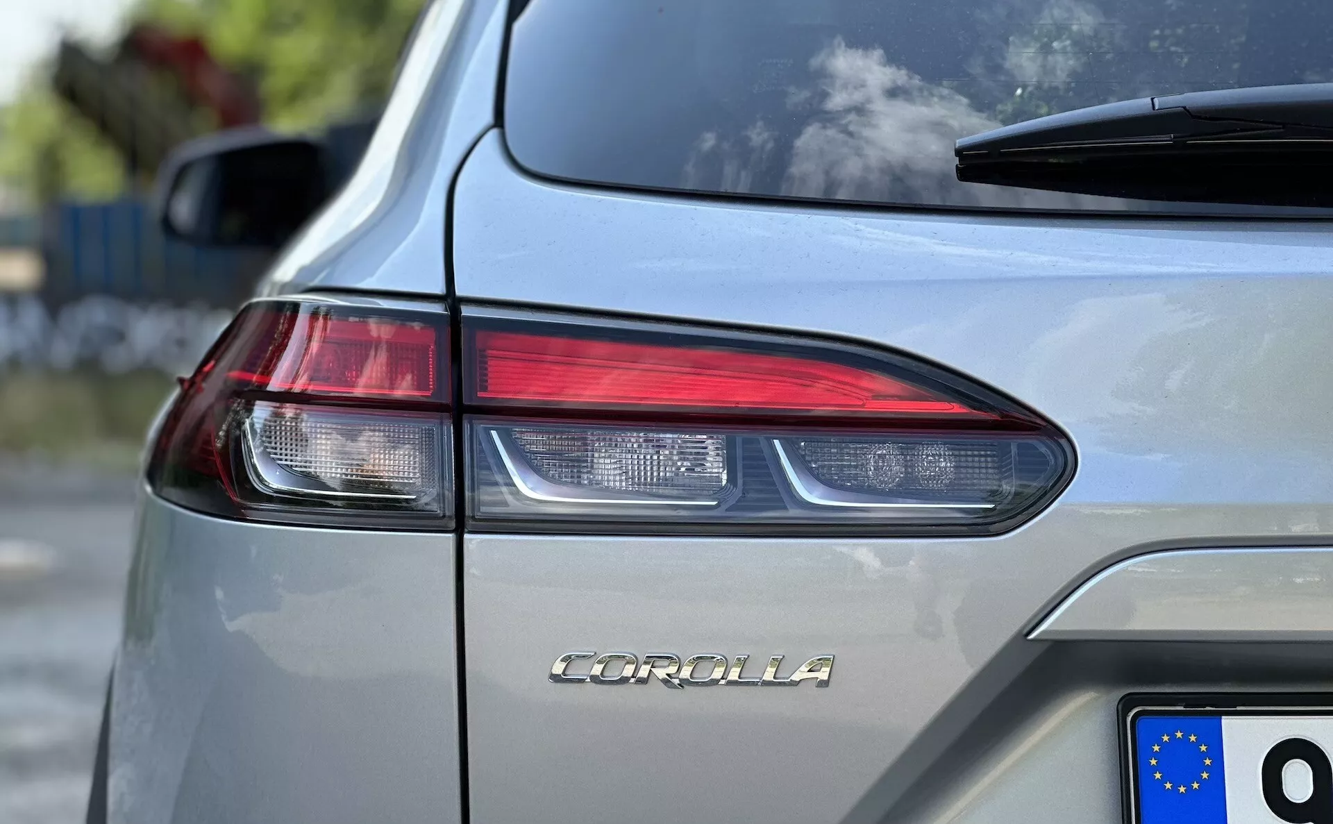 Detailný obrázok Toyota Corolla Cross 2022 so zobrazeným názvom modelu na batožinovom priestore, zameraný na dizajn uhlových LED zadných svetiel a registračnú značku Európskej únie na striebornom metalickom tele