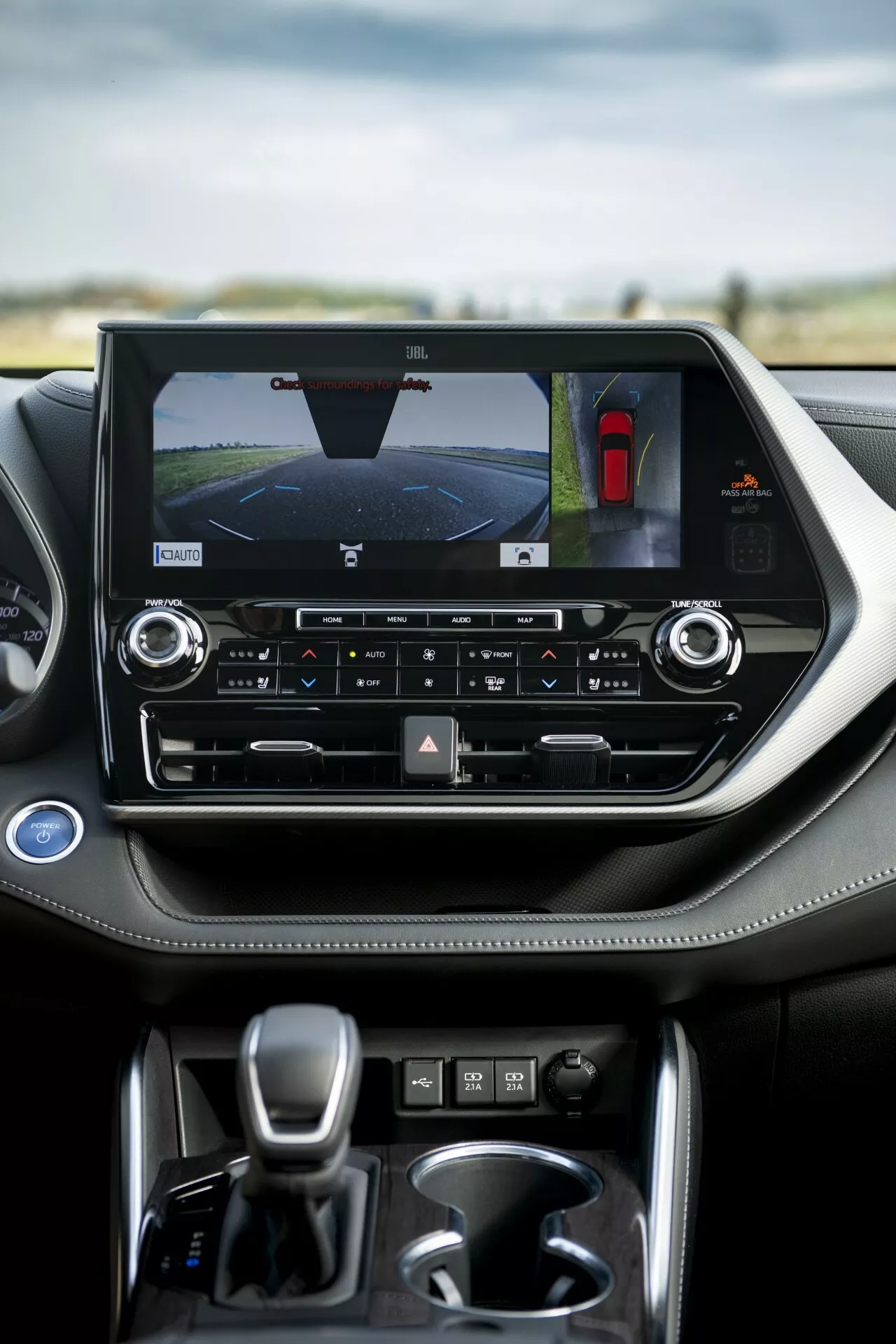 Interiér Toyoty Highlander 2021 so zameraním na stredovú konzolu s displejom orientovaným na šírku, zobrazujúcim zadnú kameru a asistenčný systém pri parkovaní, ovládanie klímy pre viac zón a automatickú prevodovku