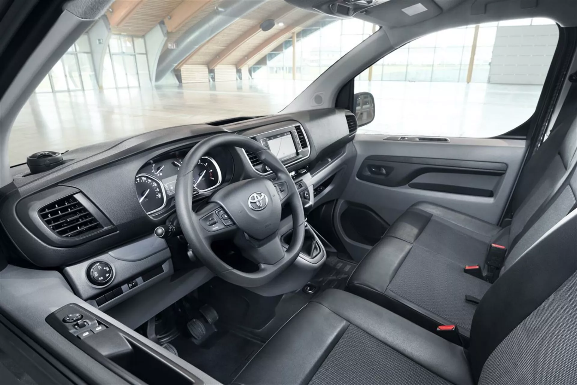 Detailný pohľad na interiér vozidla Toyota Proace Verso 2016 zameraný na stranu vodiča s detailným pohľadom na palubnú dosku, volant s logom Toyota a ovládacími prvky, prístrojový panel a systém infotainment