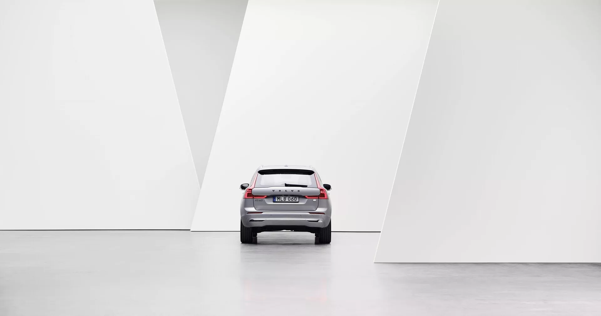 Pohľad zo stredu zadnej časti auta ukazujúci moderné dizajnové prvky, vrátane LED zadných svetiel, zadného okna, veka kufra a zadného nárazníka v minimalistickom, svetlom a symetrickom prostredí s lesklými podlahami a geometrickými bielymi stenami.