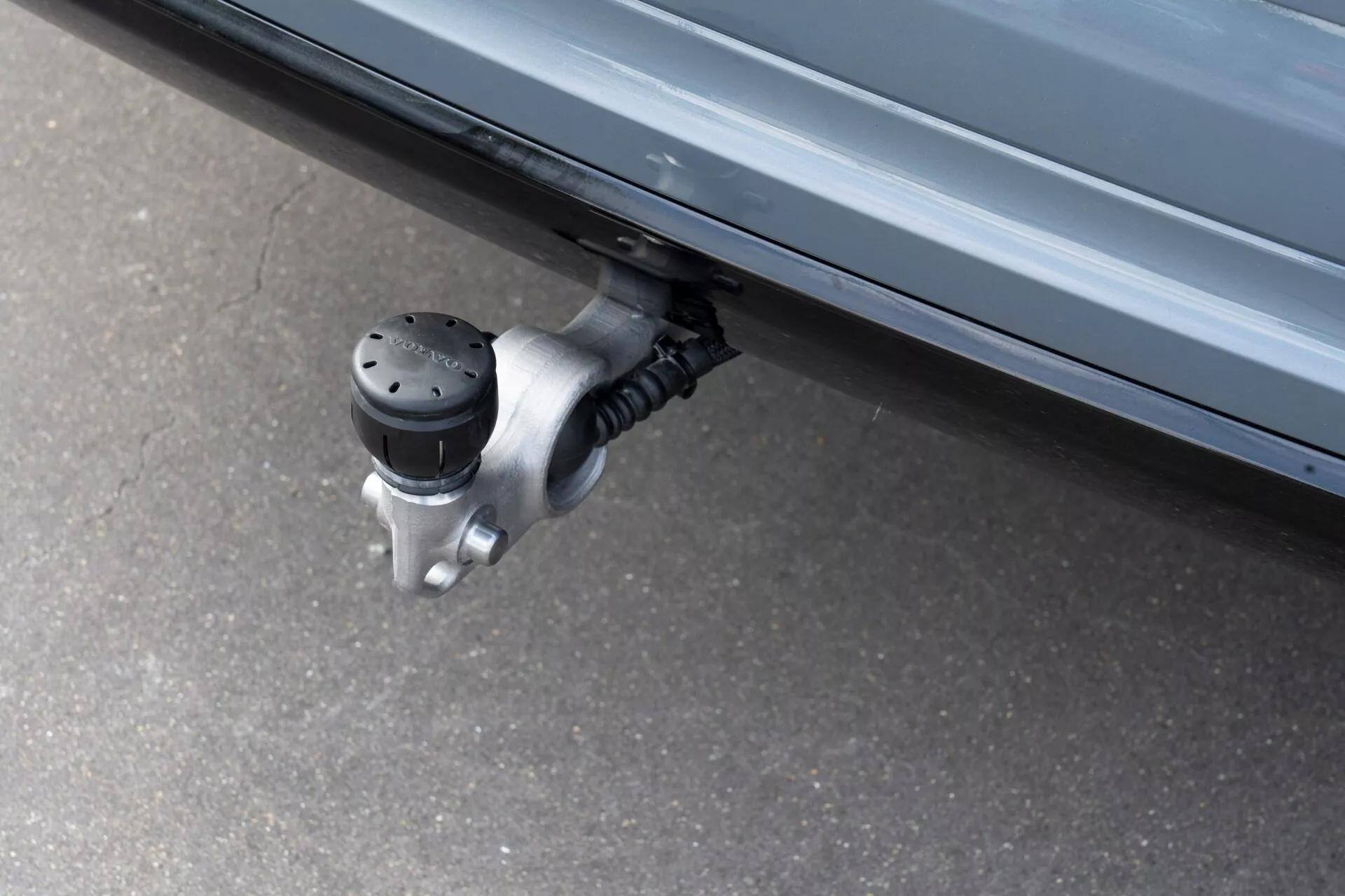 Detailný pohľad na vysúvací bočný schod vozidla Volvo XC60 2021 (2. generácia-facelift), zachytávajúci rozšírený protišmykový povrch s vyvýšenými čiernymi bodmi pod bočnými dverami vozidla, pripevnený k mechanizmu s kovovým závesom. Fotografia z nízkeho uhlu zvýrazňuje automatizovanú funkciu určenú na uľahčenie vstupu a výstupu znižovaním vzdialenosti k zemi.