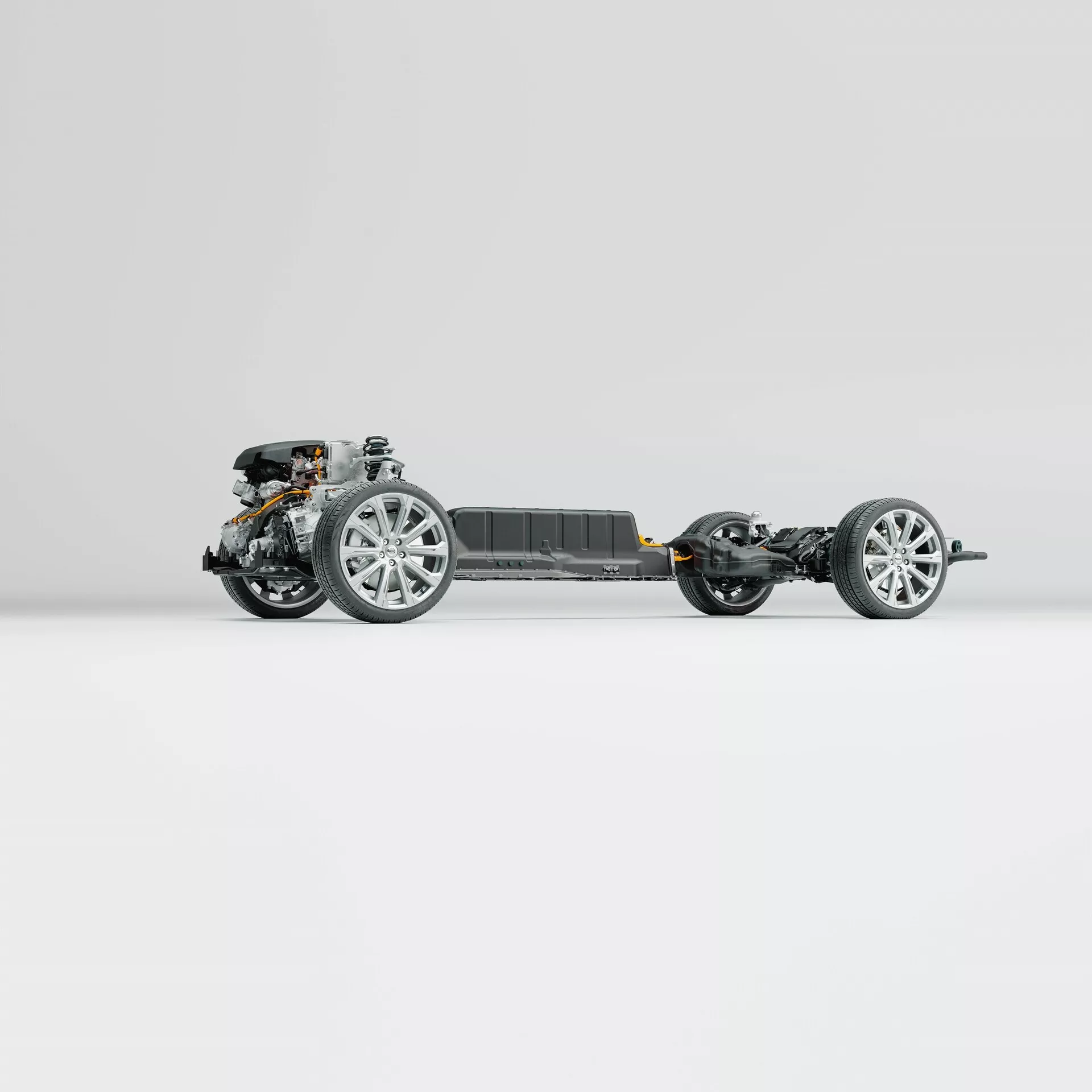 Bočný profil podvozku modelu Volvo XC60 2021 (druhé generácie-facelift). Obrázok zdôrazňuje rám vozidla, kolesá vybavené modernými zliatinovými ráfikmi, komponenty zavesenia, hnacie ústrojenstvo vpredu a centrálnu batériu, všetko na čistom neutrálnom pozadí. Fotografia odhaľuje špičkovú inžiniersku prácu bez karosérie alebo interiérových komponentov.