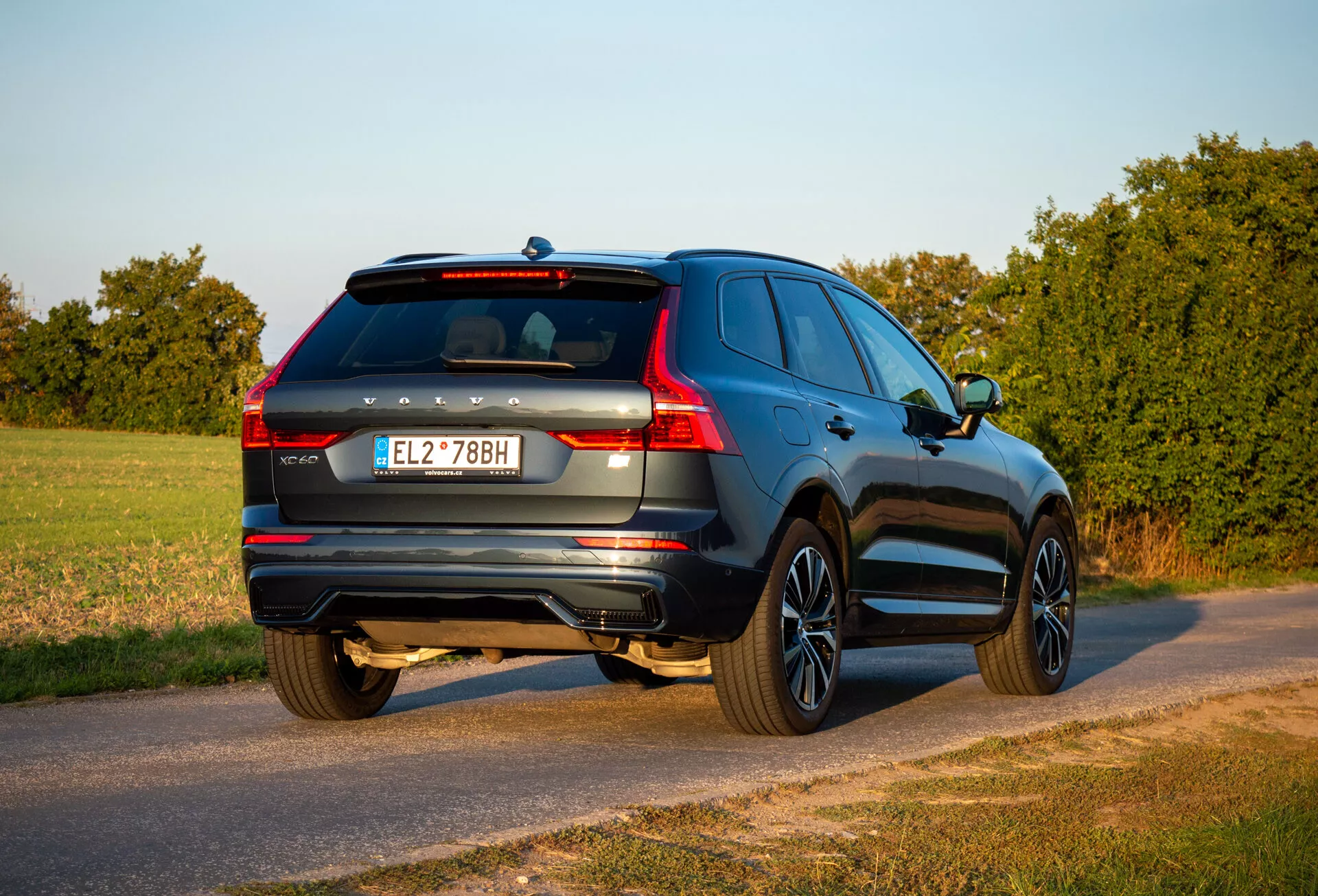 SUV Volvo XC60 Recharge plug-in hybrid z roku 2021 v pohľade z troch štvrtín zozadu zaparkované na vidieckej ceste počas zlatého hodiny s viditeľným zadným koncom, stranou pasažiera, detailmi kufra a dizajnovými prvkami