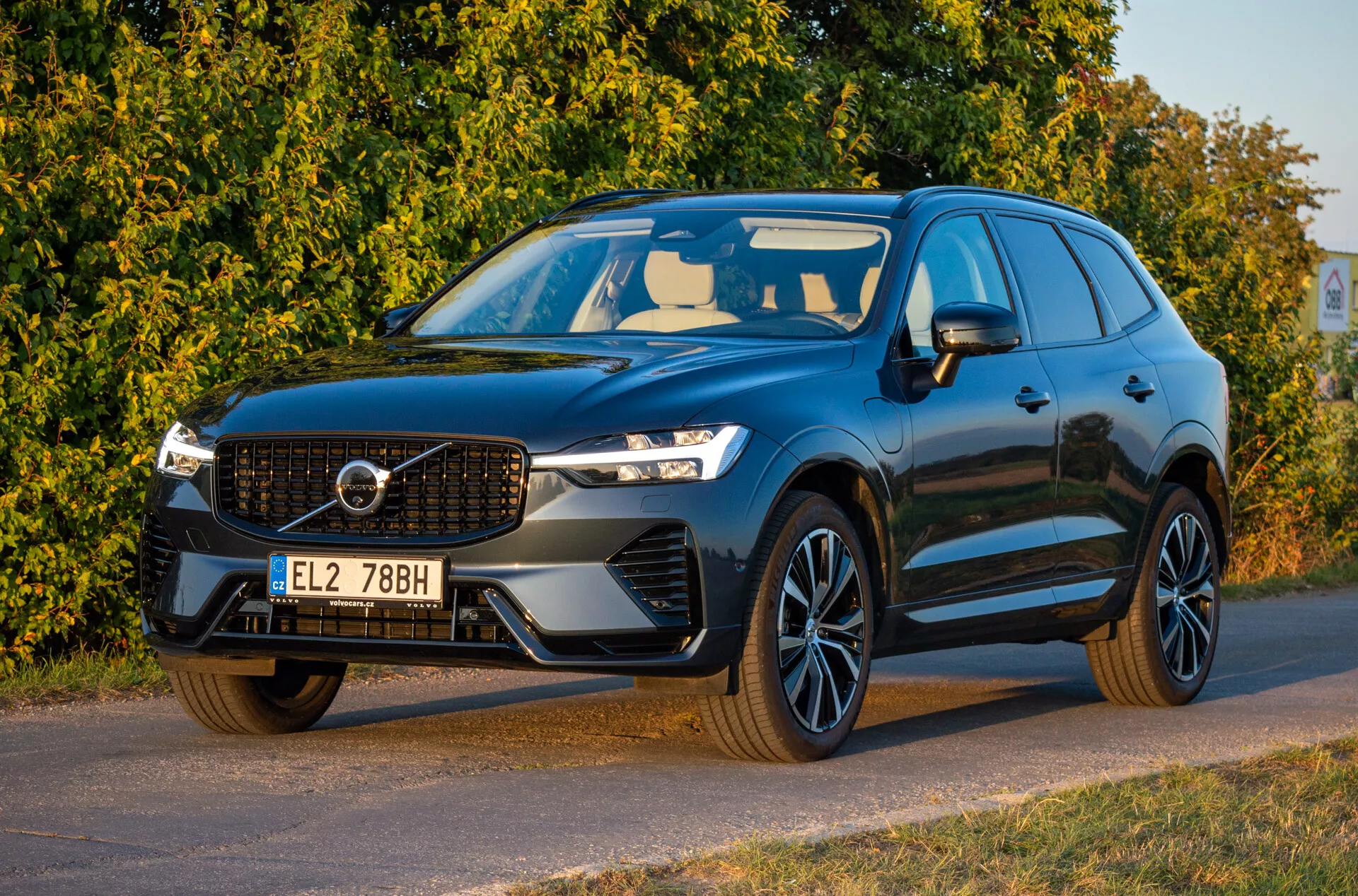 Volvo XC60 Recharge plug-in hybrid z roku 2021 v tmavej farbe, zobrazenie z trojštvrťového predného uhla s LED svetlometmi, charakteristickou mriežkou chladiča, športovými zliatinovými kolesami a aerodynamickým dizajnom, zaparkované diagonálne orientované doľava so detailným pohľadom na prednú časť a stranu vodiča.