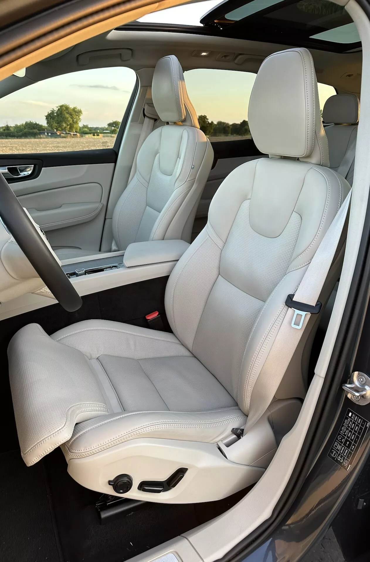 Interiér Volvo XC60 Recharge plug-in hybrid 2021: predné a čiastočne zadné sedadlá, luxusné svetlofarebné kožené čalúnenie, moderný dizajn, elektricky nastaviteľné sedadlá s elegantnými švami, záber zvonka dverí na strane spolujazdca pri dennom svetle