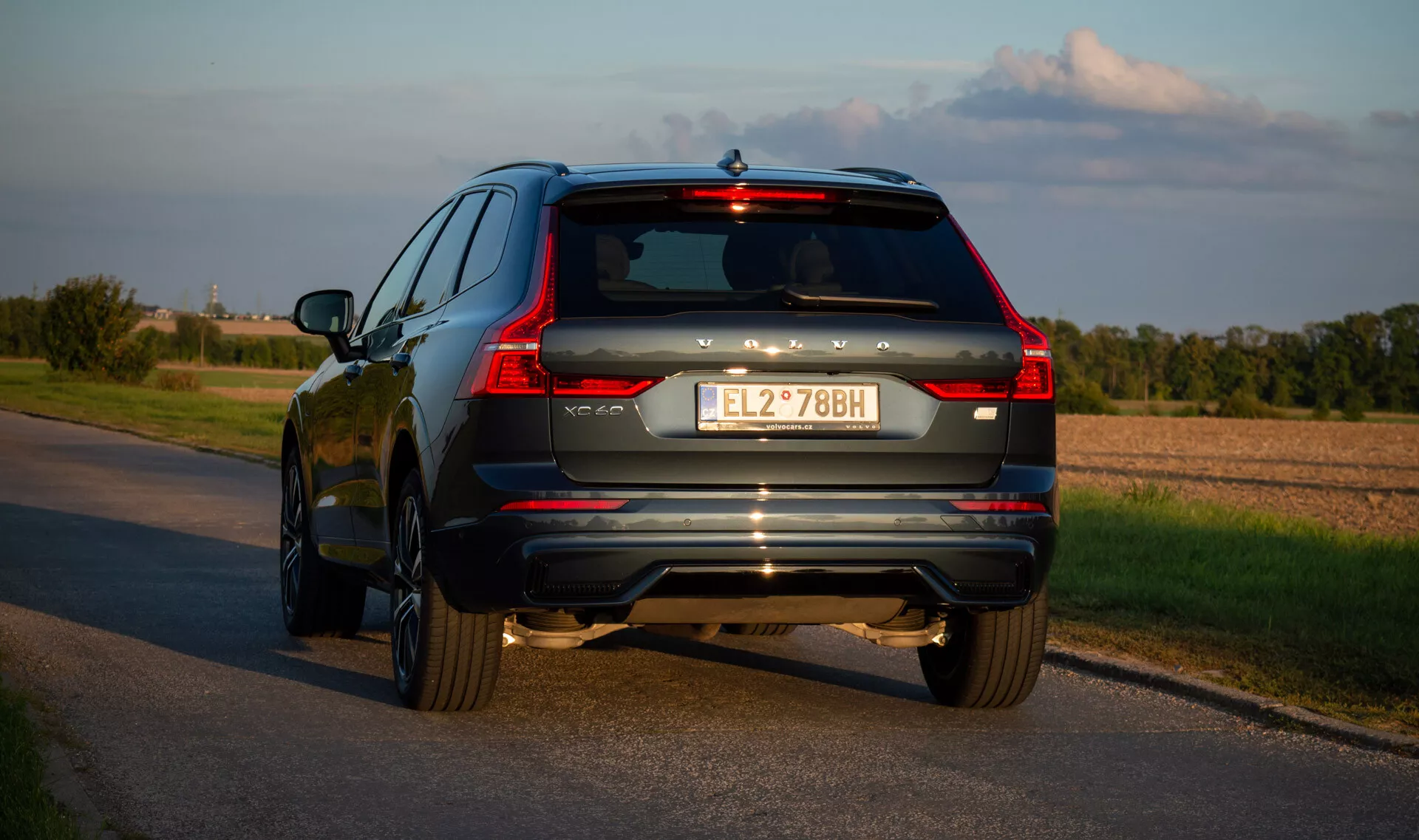 SUV Volvo XC60 Recharge plug-in hybrid 2021 na asfaltovej ceste, zachytené z trojštvrtečného zadného uhla zdôrazňujúce LED zadné svetlá vozidla, výfukový systém a chrómové doplnky počas neskorého popoludnia