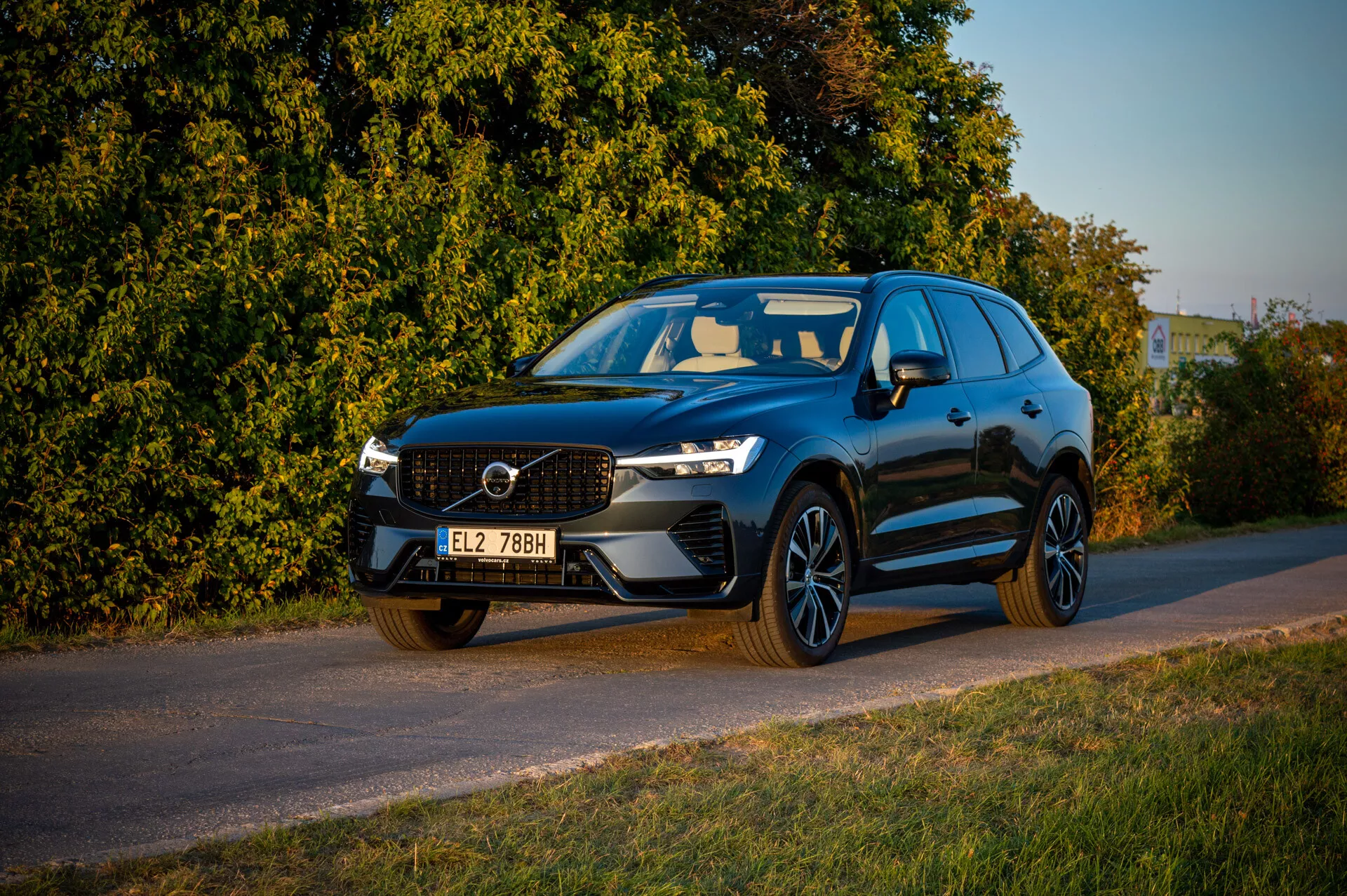 Volvo XC60 Recharge Plug-In Hybrid z roku 2021 zaparkované pri ceste počas neskorého popoludnia s teplým osvetlením, zobrazujúce prednú mriežku, LED svetlomety a športový profil na pozadí vegetácie
