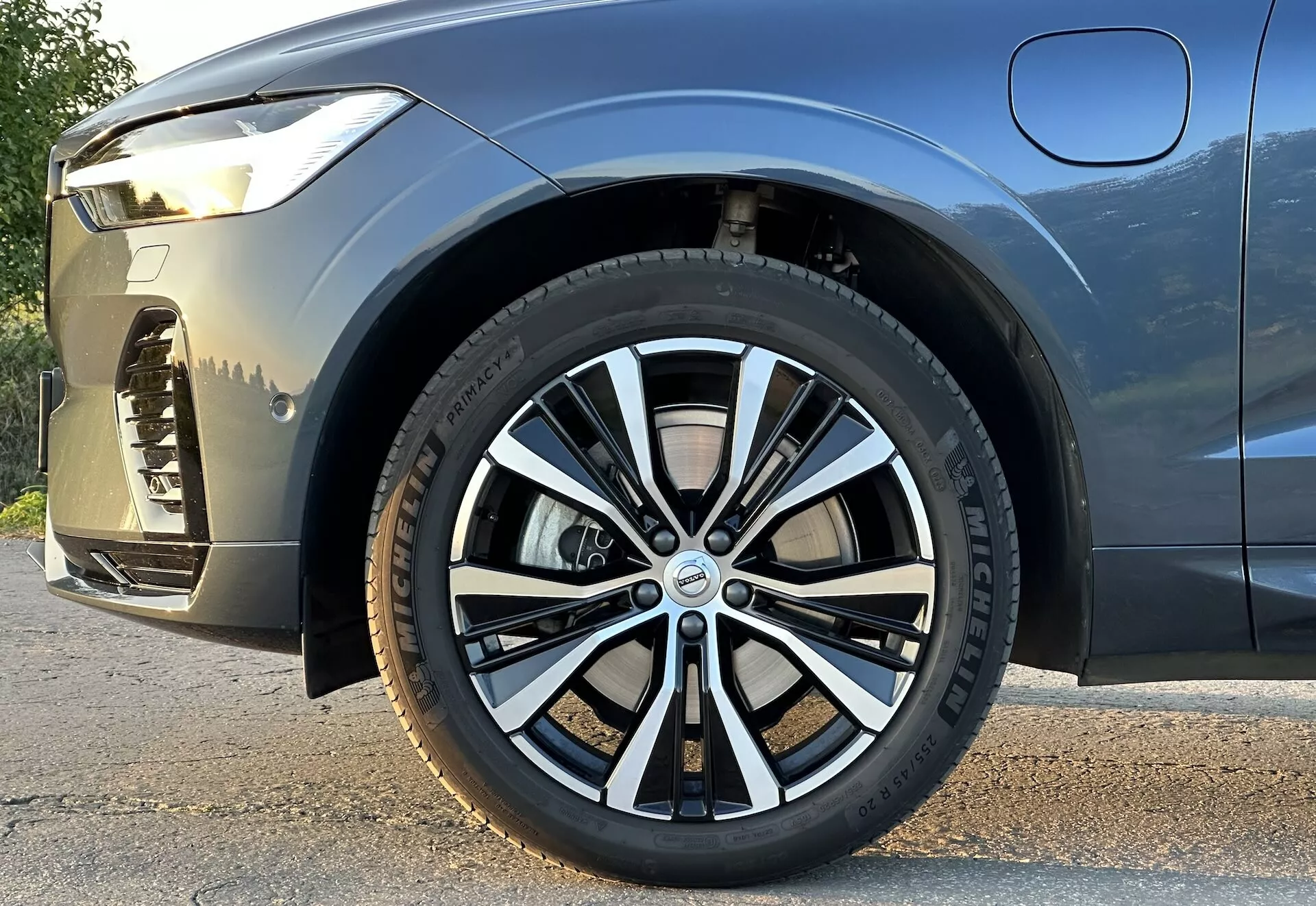 Detailný pohľad z nízkeho uhla na Volvo XC60 Recharge Plug-In Hybrid 2021 so zameraním na predné koleso a bok vozidla, zdôrazňujúci dizajn kolesa, dezén pneumatiky a postoj vozidla