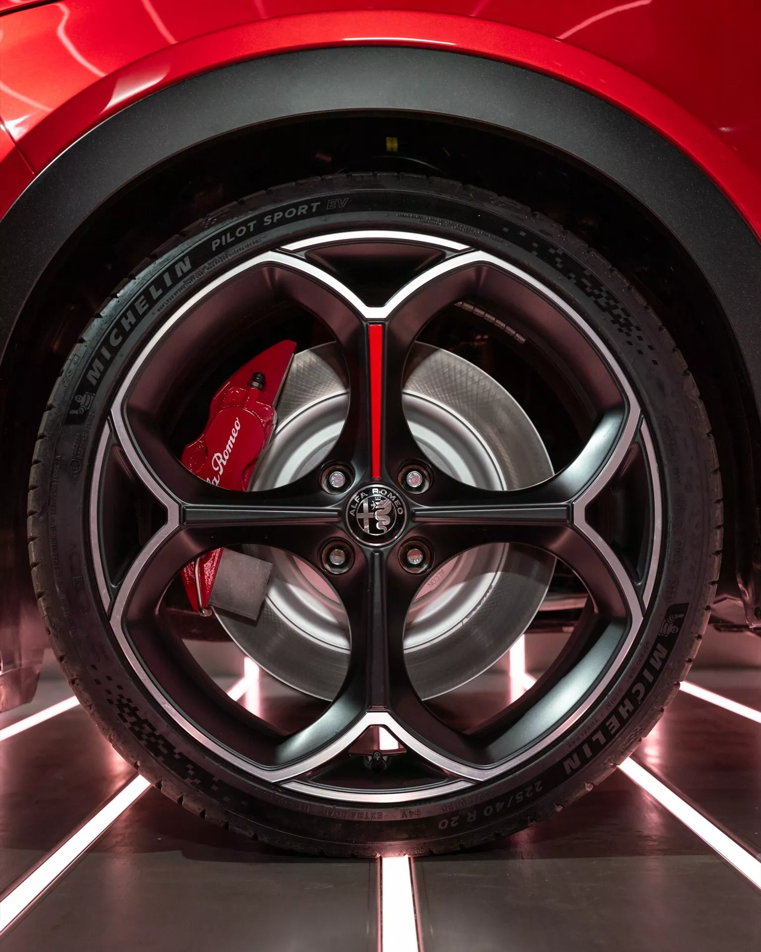 Detailný záber na koleso Alfa Romeo Junior 2024 s prepracovaným dizajnom disku a pneumatikou Michelin Pilot Sport 4 v prostredí showroomu, zdôrazňujúci výkon a športovú estetiku