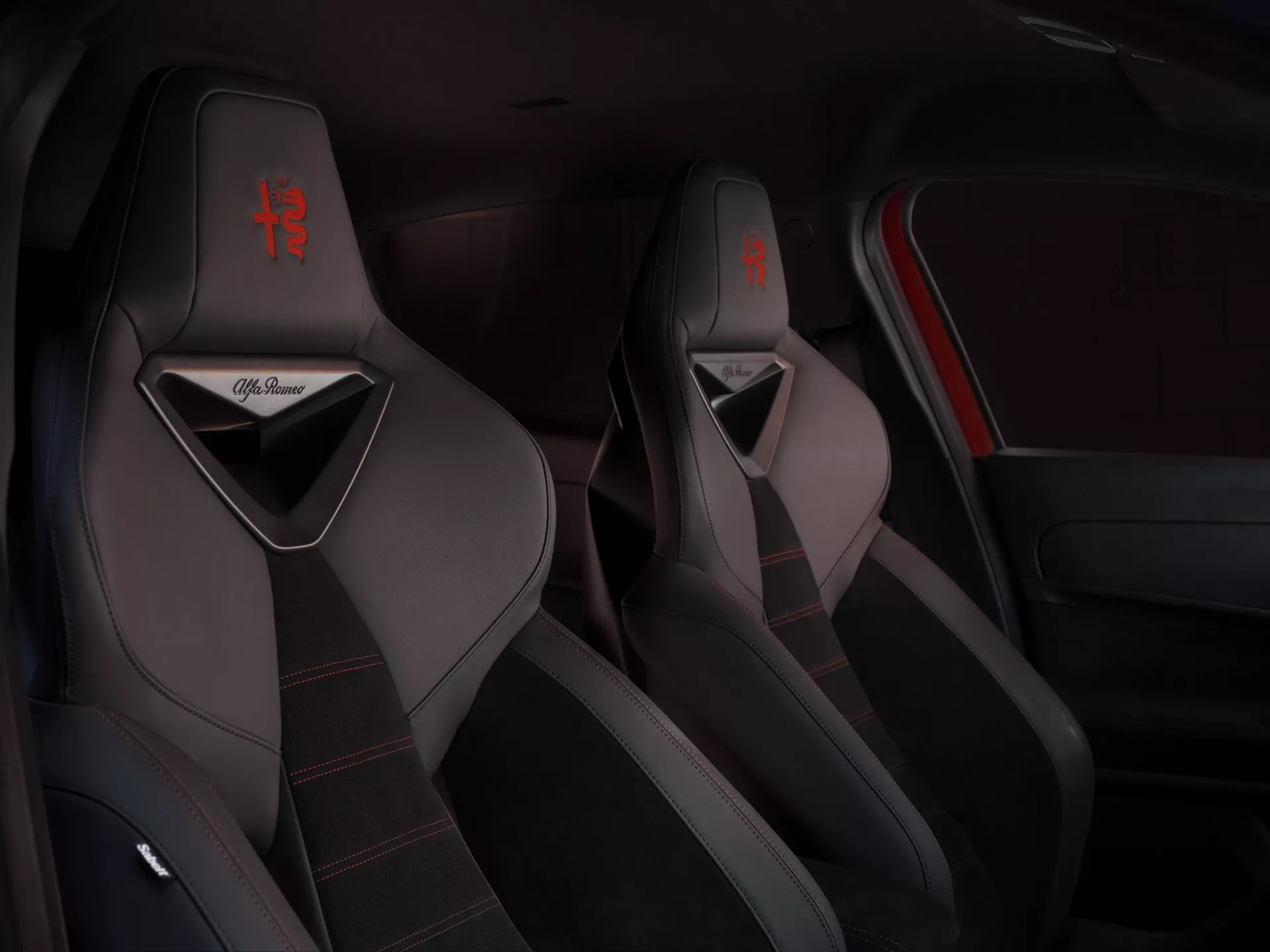 Pohľad na interiér Alfa-Romeo Junior 2024 zameraný na športové predné sedadlá s červeným prešívaním a logom, predvádzajúci kvalitné čalúnenie a športové dizajnové prvky
