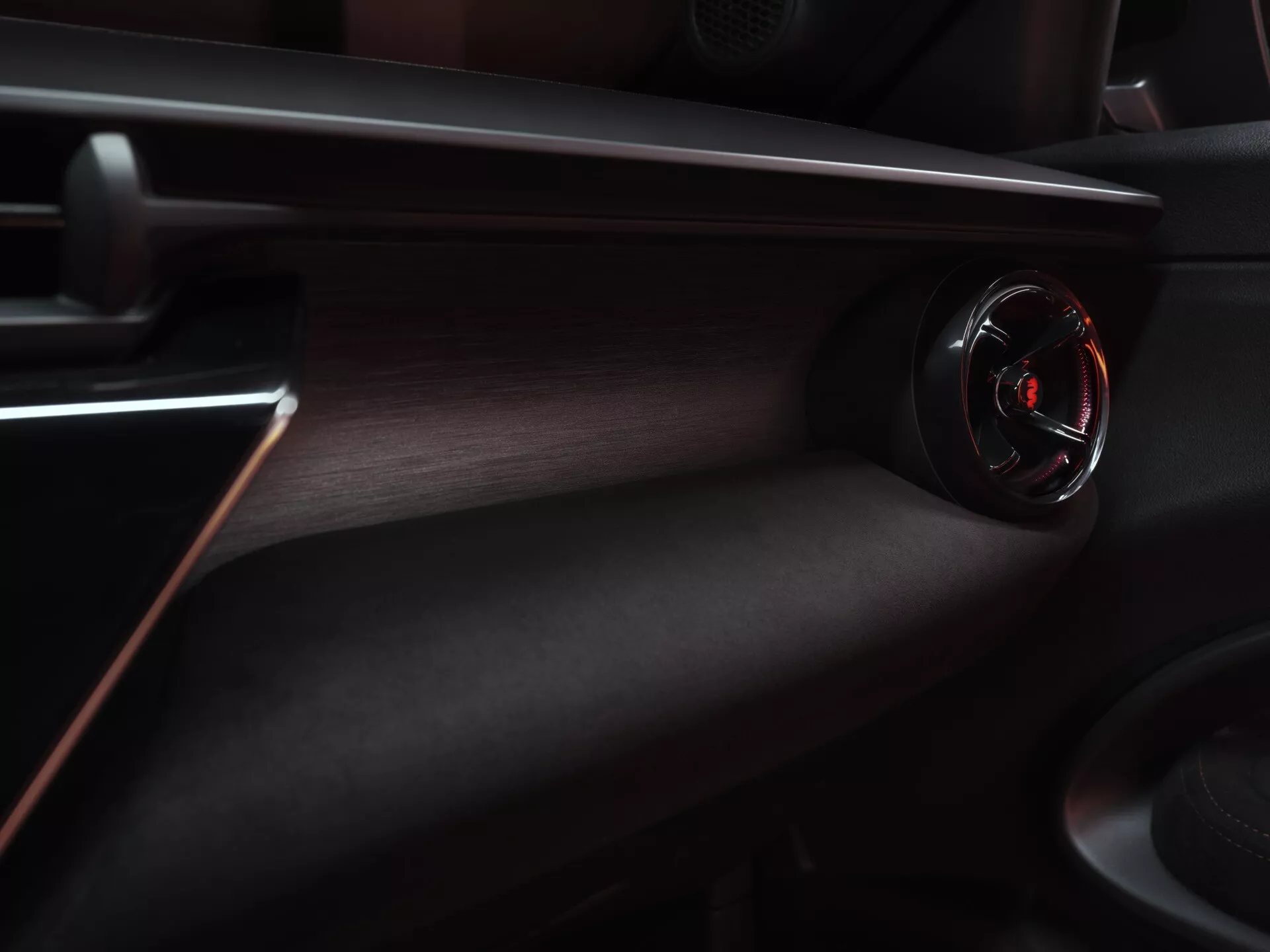 Interiérový pohľad na Alfa Romeo Junior 2024, zdôrazňujúci palubnú dosku na strane spolujazdca s kruhovou ventiláciou s lesklým čiernym povrchom a červeným akcentom, obklopený luxusnou tmavo textúrovanou palubnou doskou s červeným dekoračným prešívaním